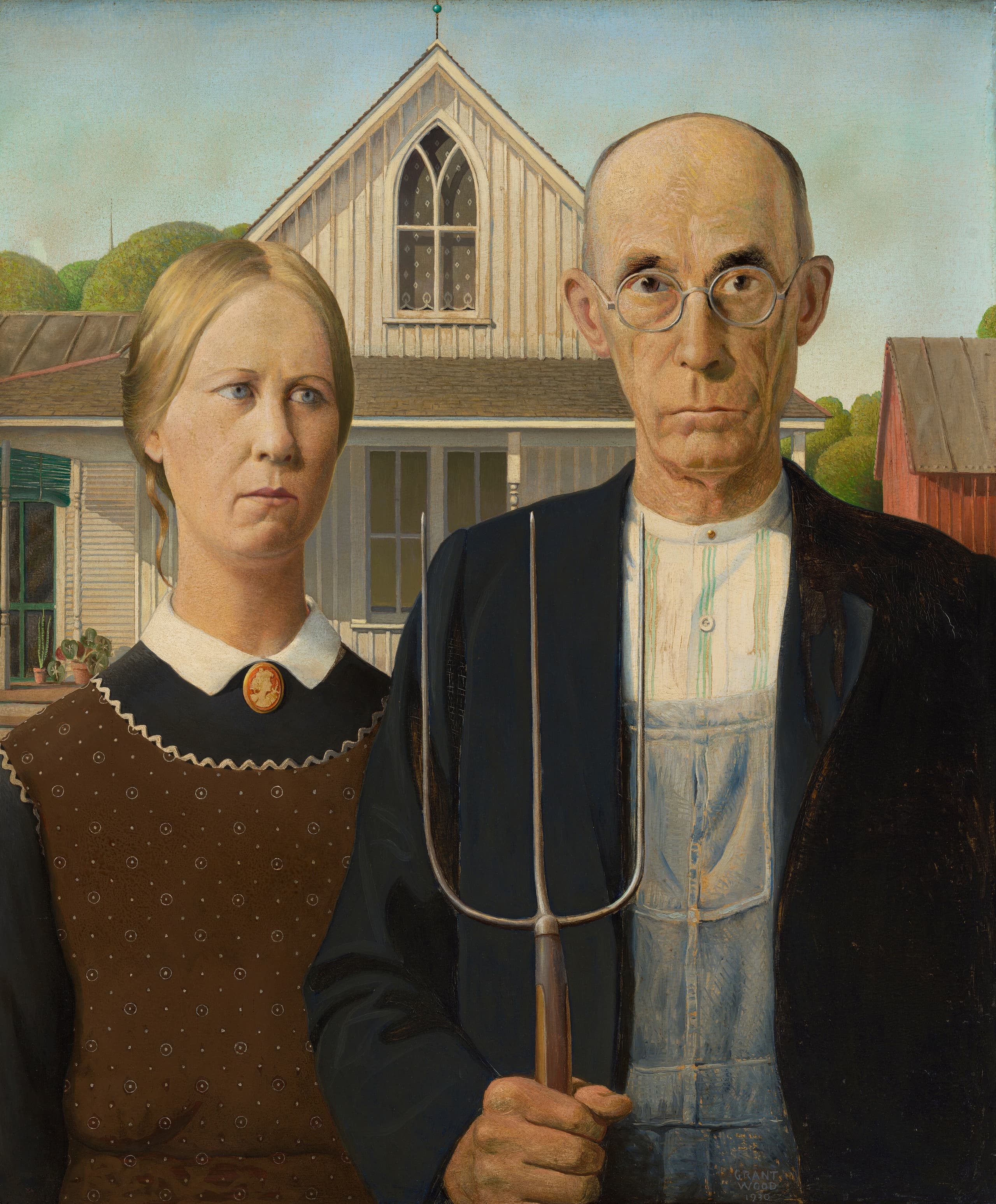 A man holding a three-tined pitchfork stands beside a woman in a print apron; both face us before a white wooden house with a pointed Gothic window.