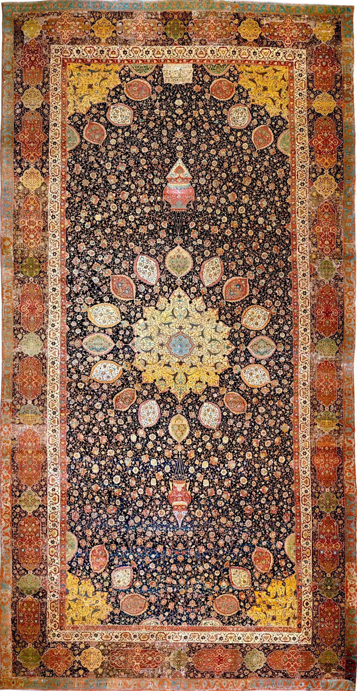 A long rectangular carpet with a central gold and blue medallion surrounded by ornate floral and geometric patterns in red, blue, green, and cream, with two hanging lamps woven into the design at either end.