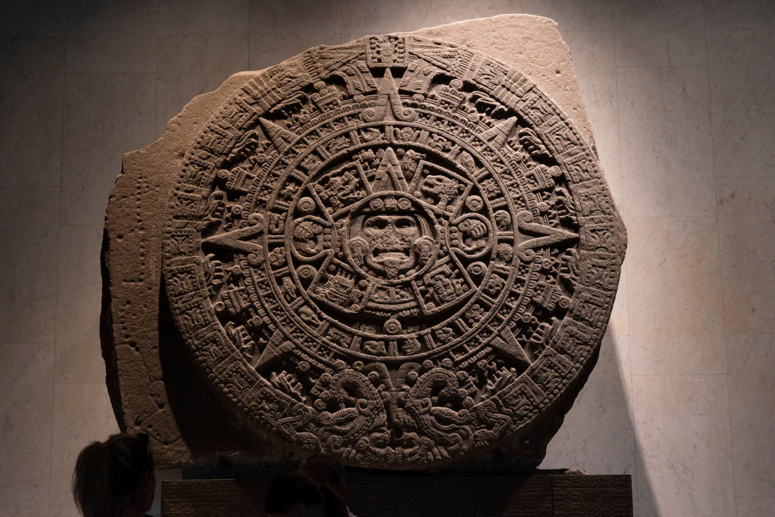 A dark circular basalt disk densely carved with a large central face and successive rings of figures and signs, shown flat and filling the frame.