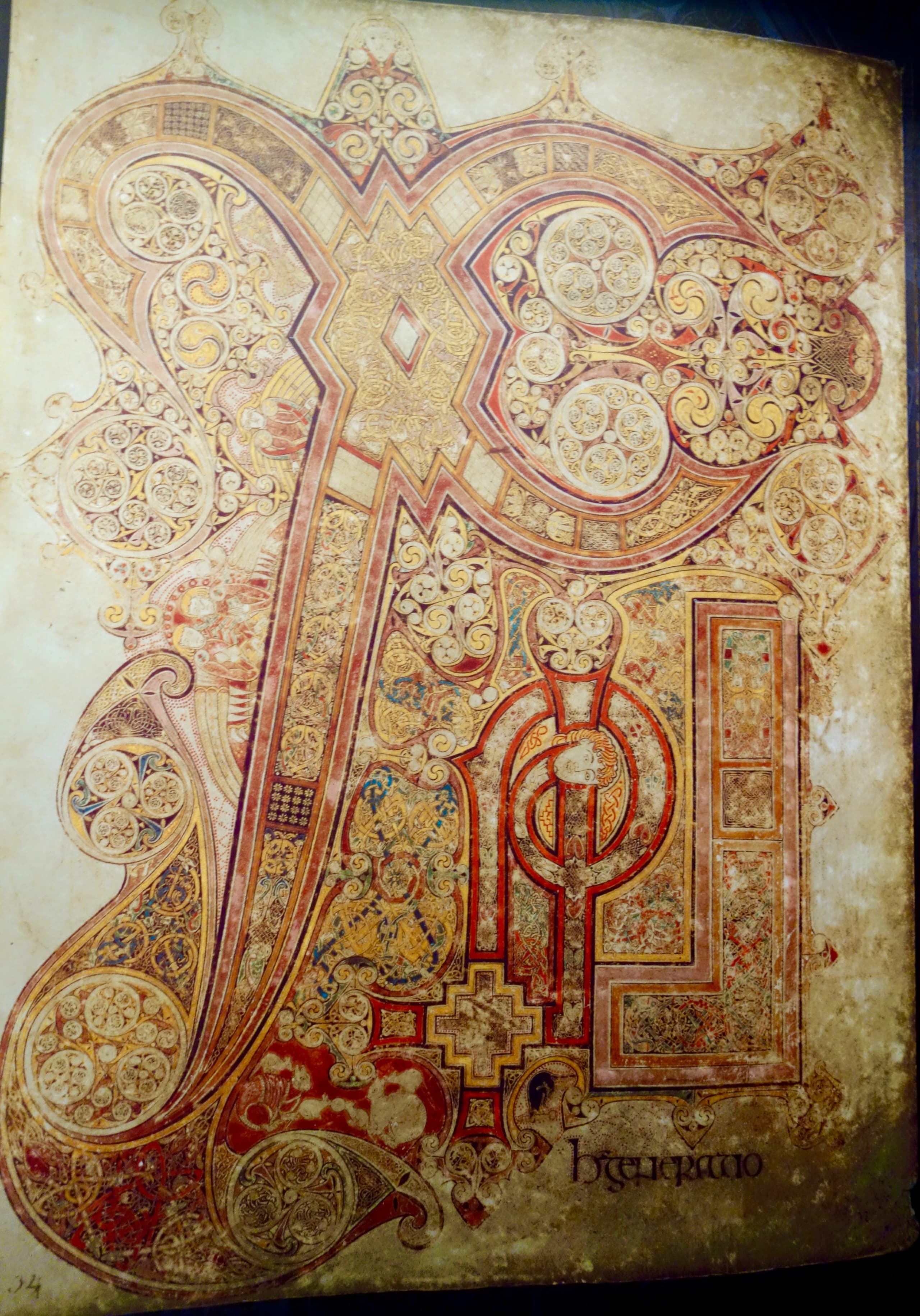 A vellum page filled almost entirely by an ornate monogram in ink and pigment. The letters are formed from spirals, interlace and geometric panels in yellow, red, blue, green and purple. Small animal forms are visible within the decoration.