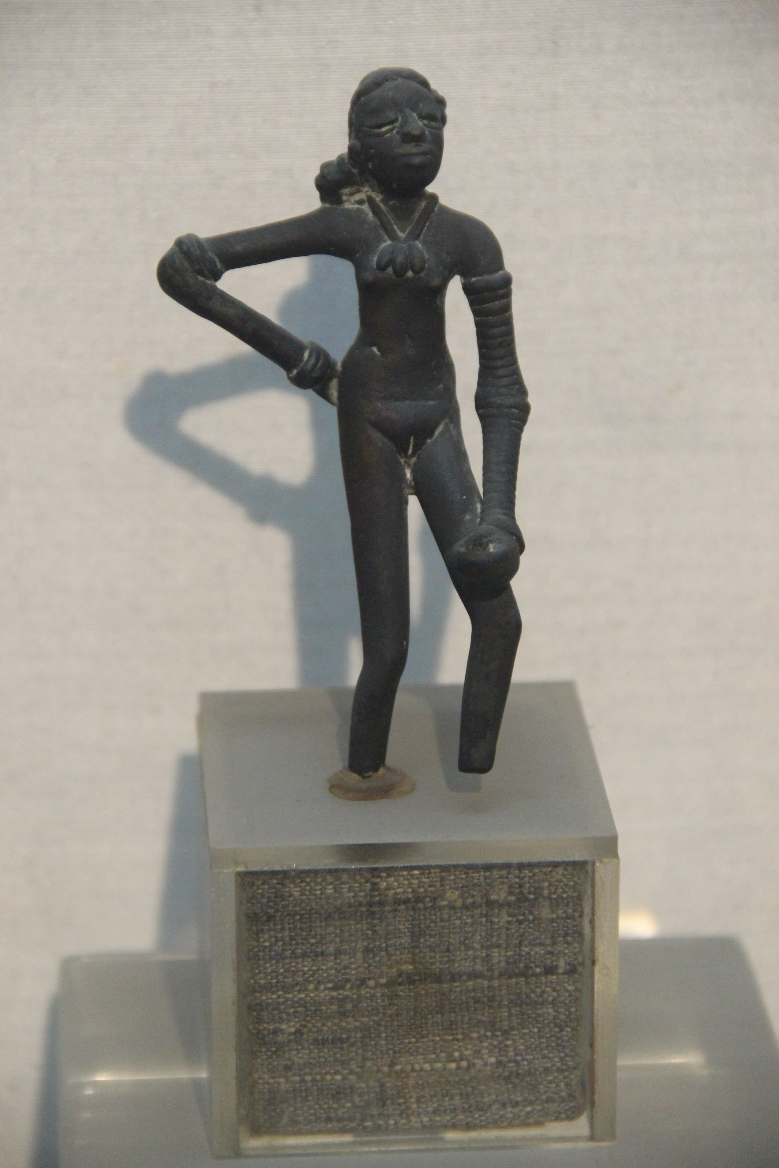 A small bronze figure standing with weight on one leg, one hand on hip, the left arm covered in stacked bangles.