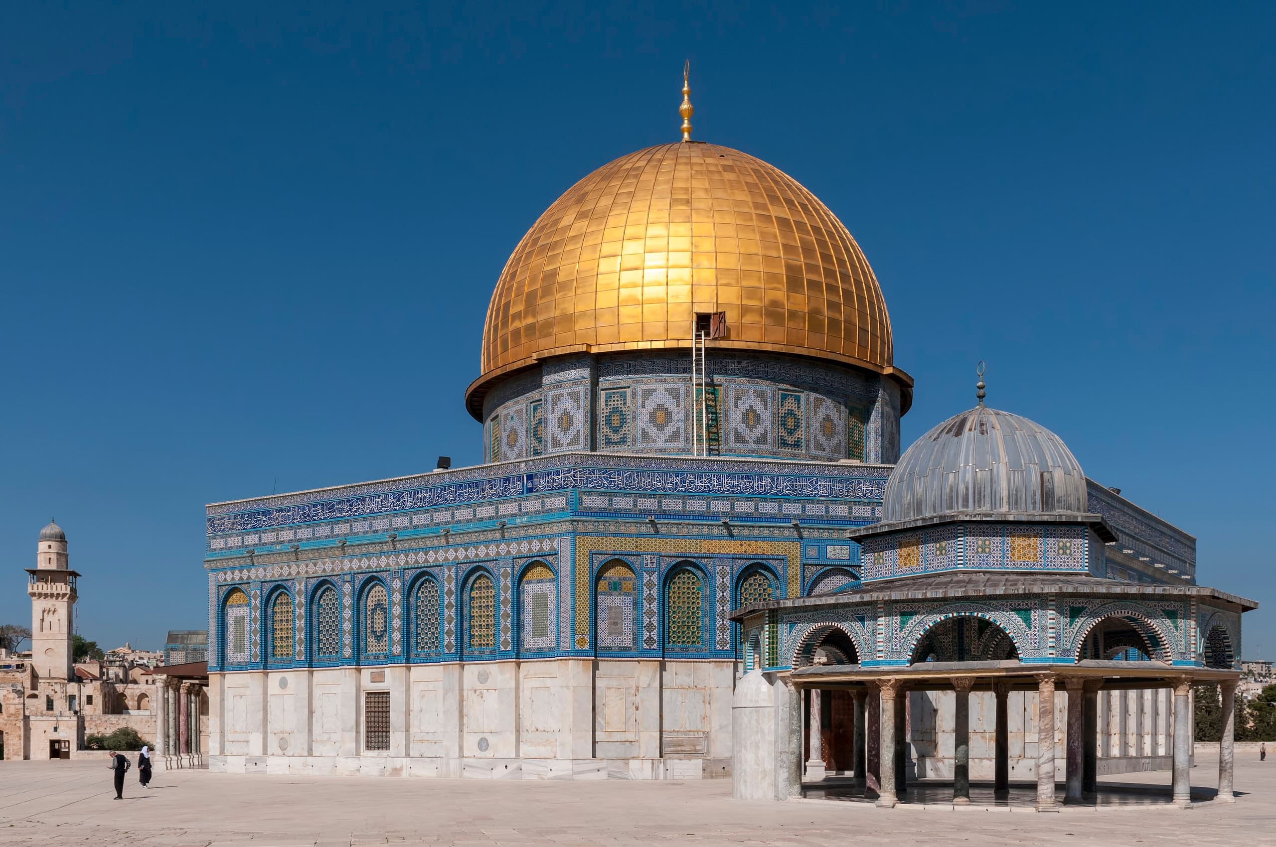 An octagonal building with a golden dome, covered in blue and white tilework, set on a raised platform with arched openings below.