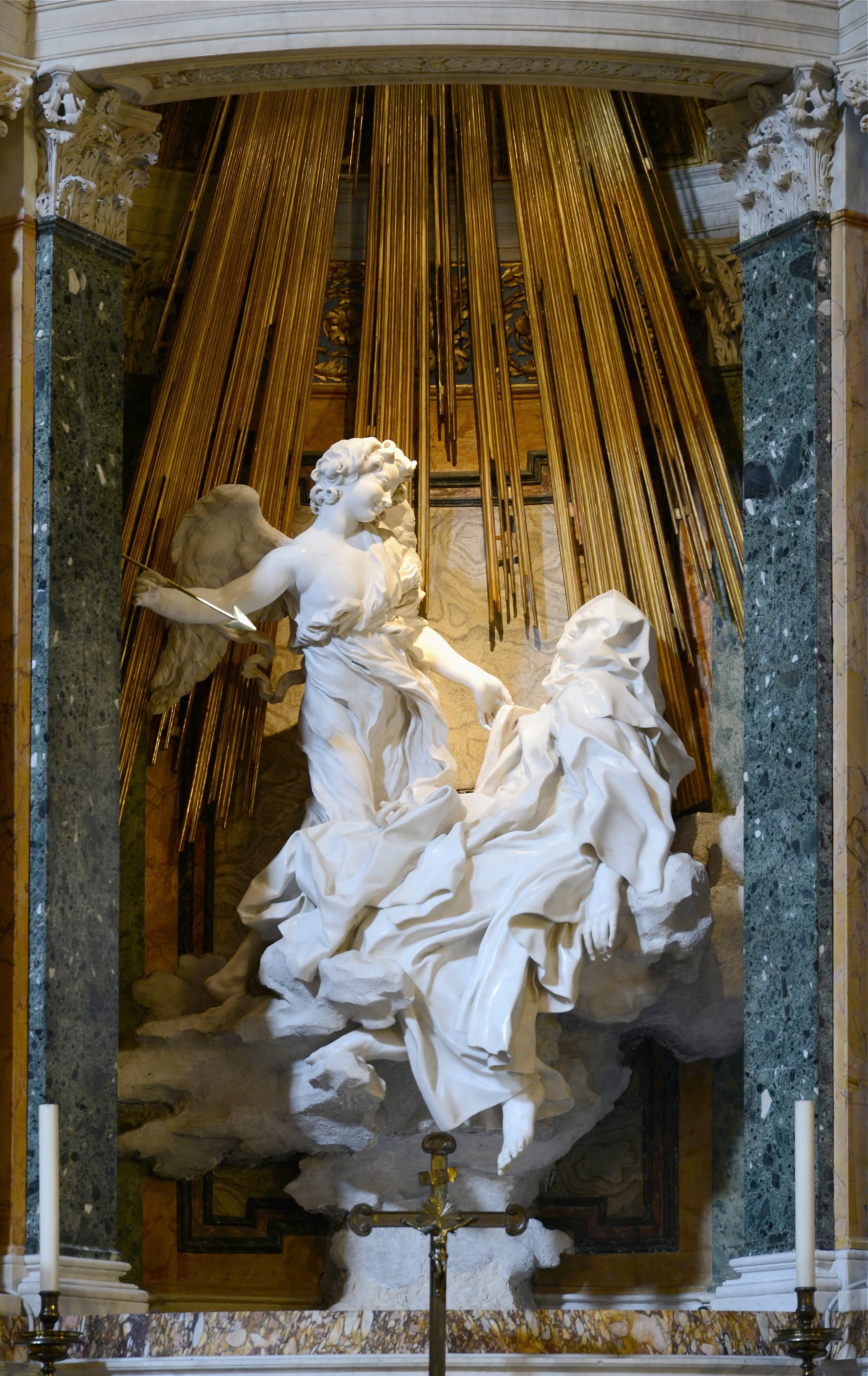 A white marble nun collapses backward on cloud-like forms as a youthful angel with a slender spear leans over her, set high within a chapel aedicule.