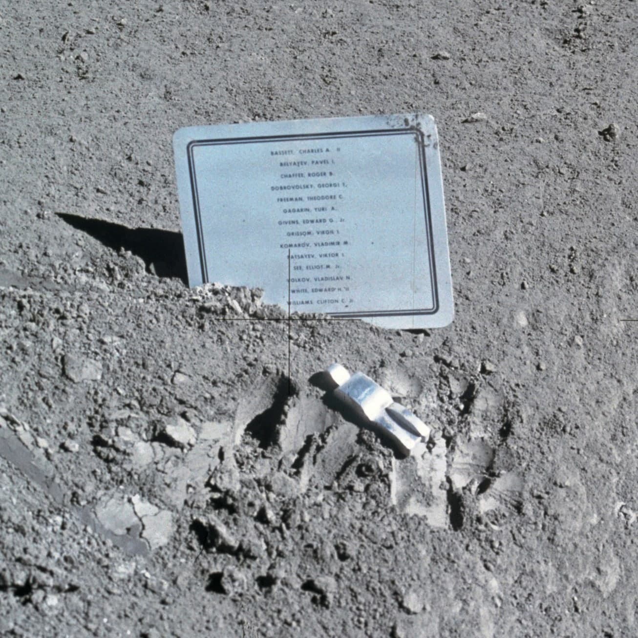 A small, pale, stylised astronaut figure lying on dusty ground among boot prints, simplified to helmet and suited limbs without facial detail.