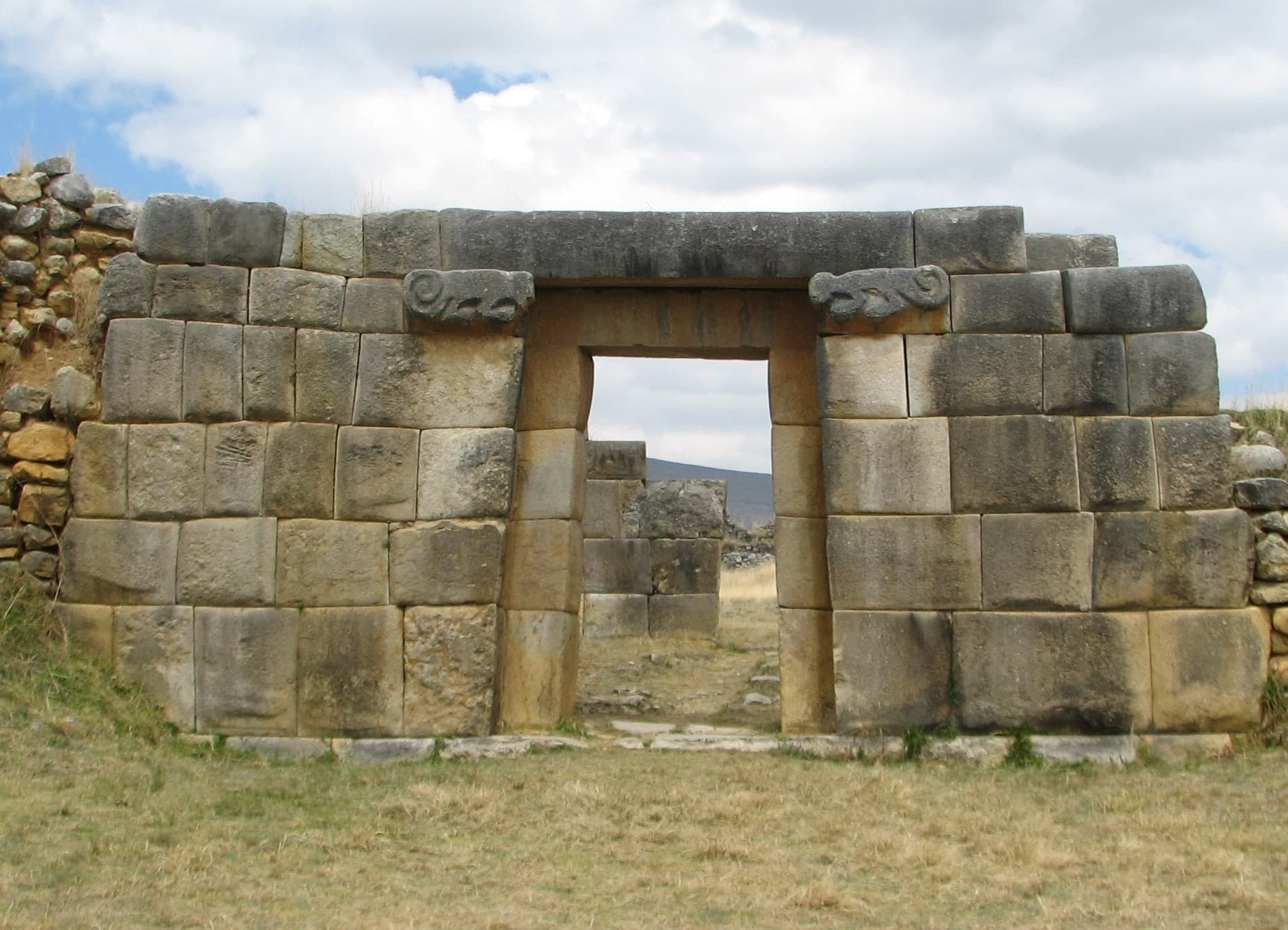 Close view of a stone wall made of irregular polygonal blocks fitted tightly together without mortar. The blocks have slightly rounded faces and recessed joints. The wall leans inward.