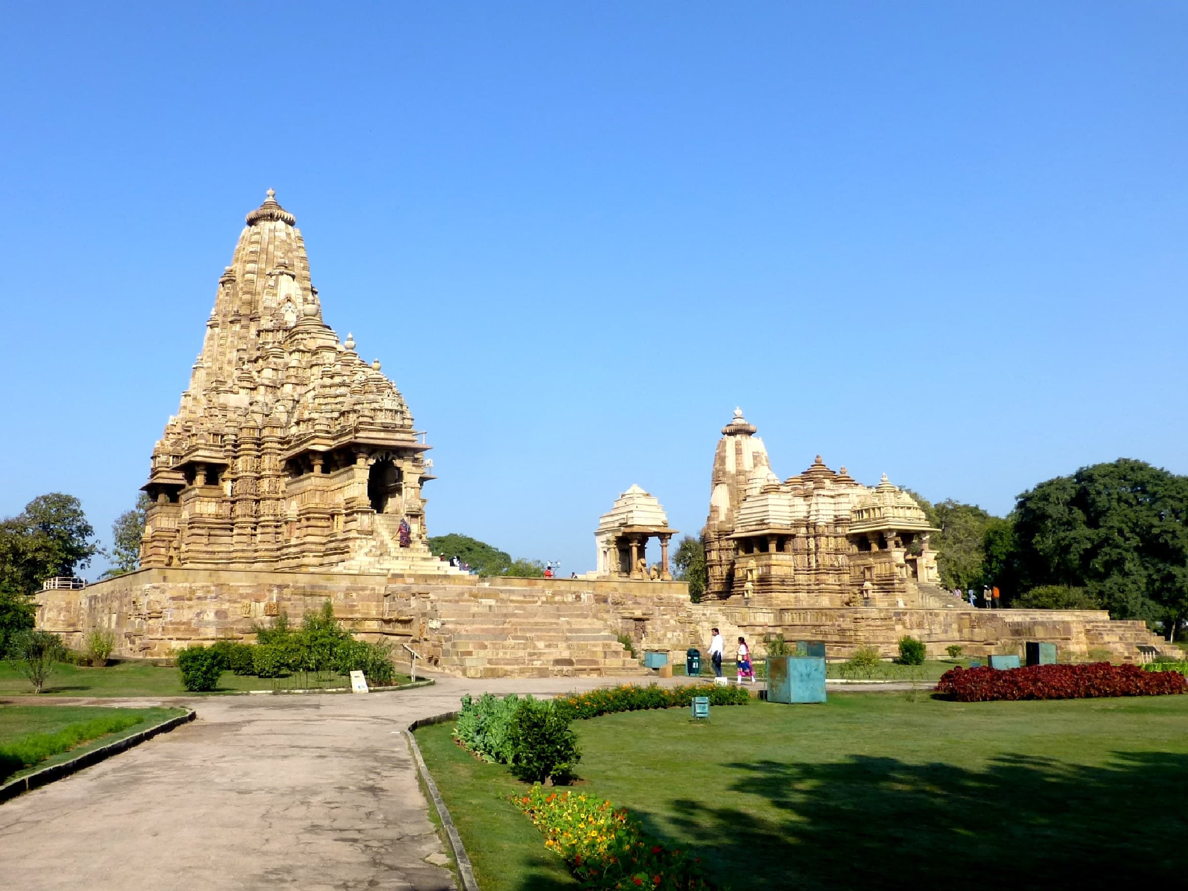 Sandstone temple exterior with multiple horizontal bands of high-relief sculpture. Figures of gods, dancers, and humans in various poses cover the wall, carved nearly free of the stone.