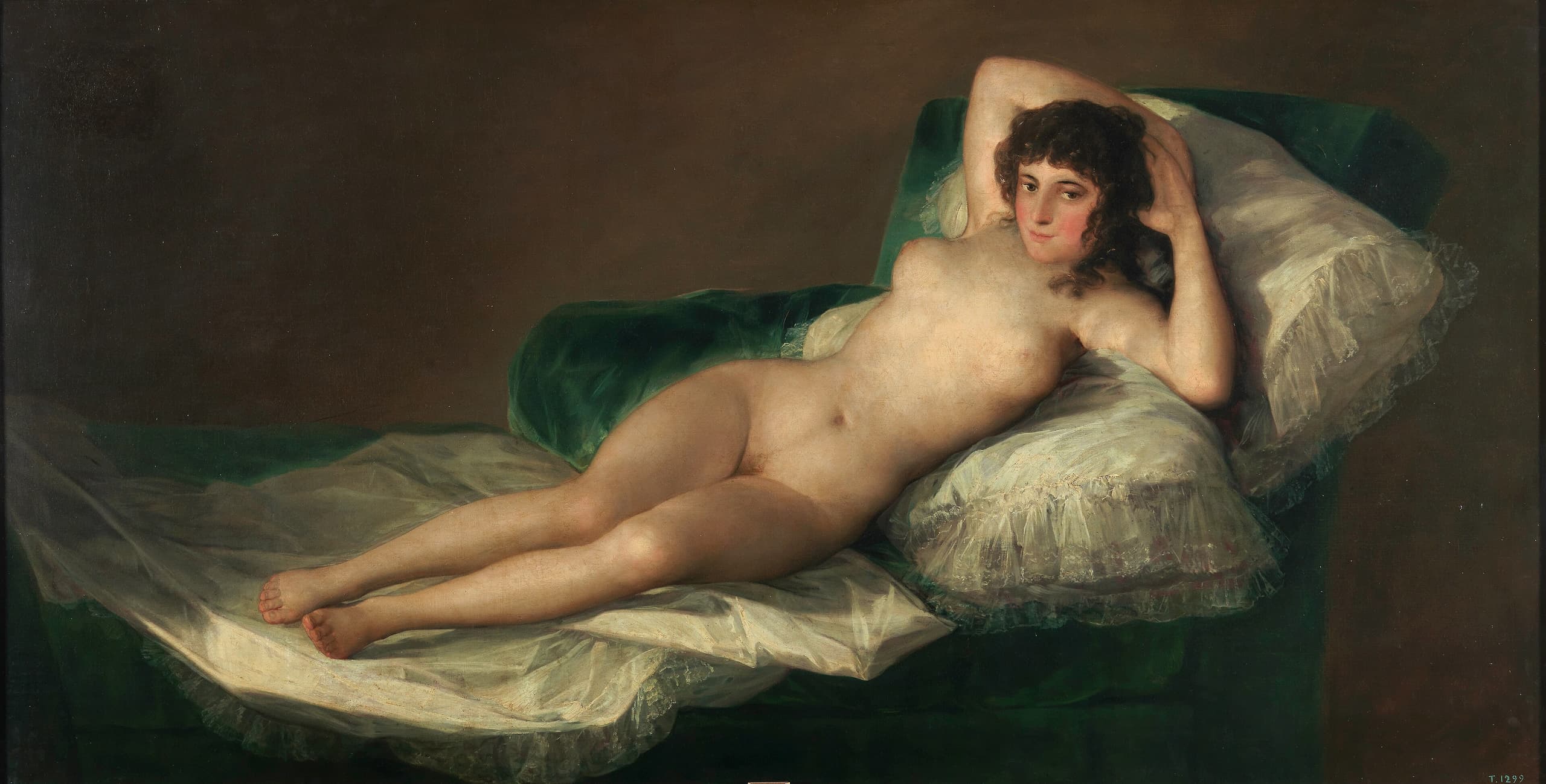 A nude woman reclines full-length on a bed of pale pillows, arms folded behind her head, looking straight out. The canvas is wide and low; the background is dark and plain.