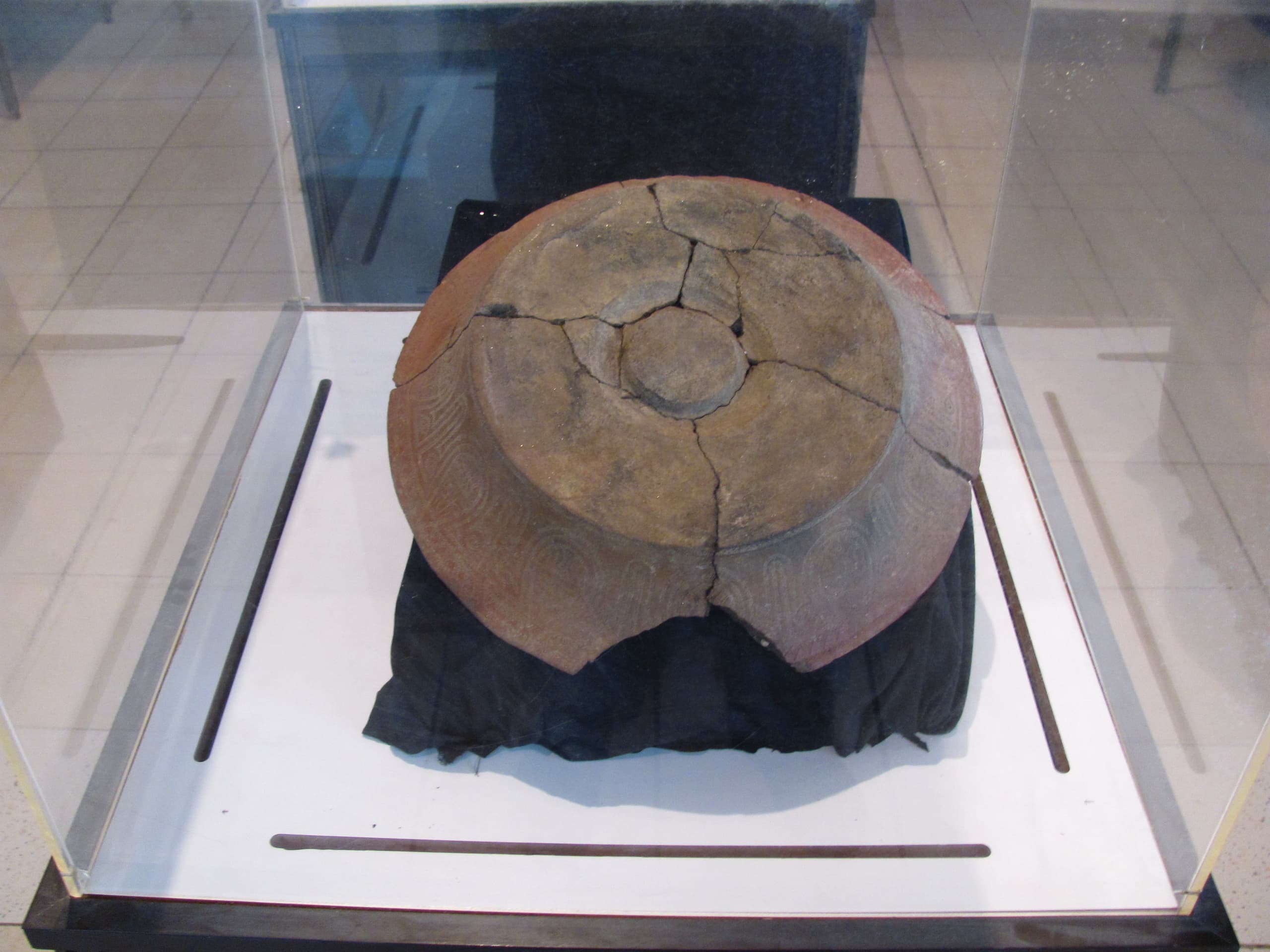 A fragment of reddish-brown earthenware with geometric patterns stamped into the surface: bands of small rectangular impressions arranged into zigzags and interlocking shapes, some filled with white lime.