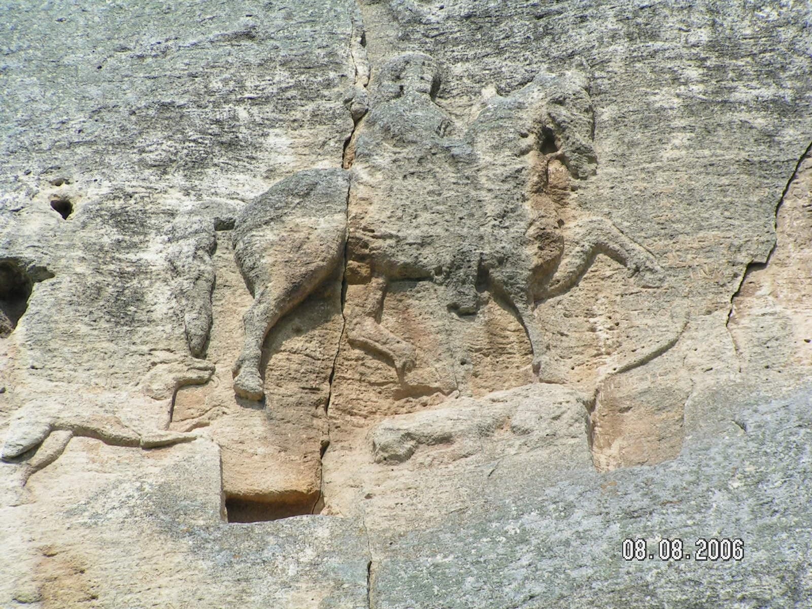 A weathered rock face carrying a large shallow relief of a horseman in profile, the figure and mount reading as one mass against the cliff.