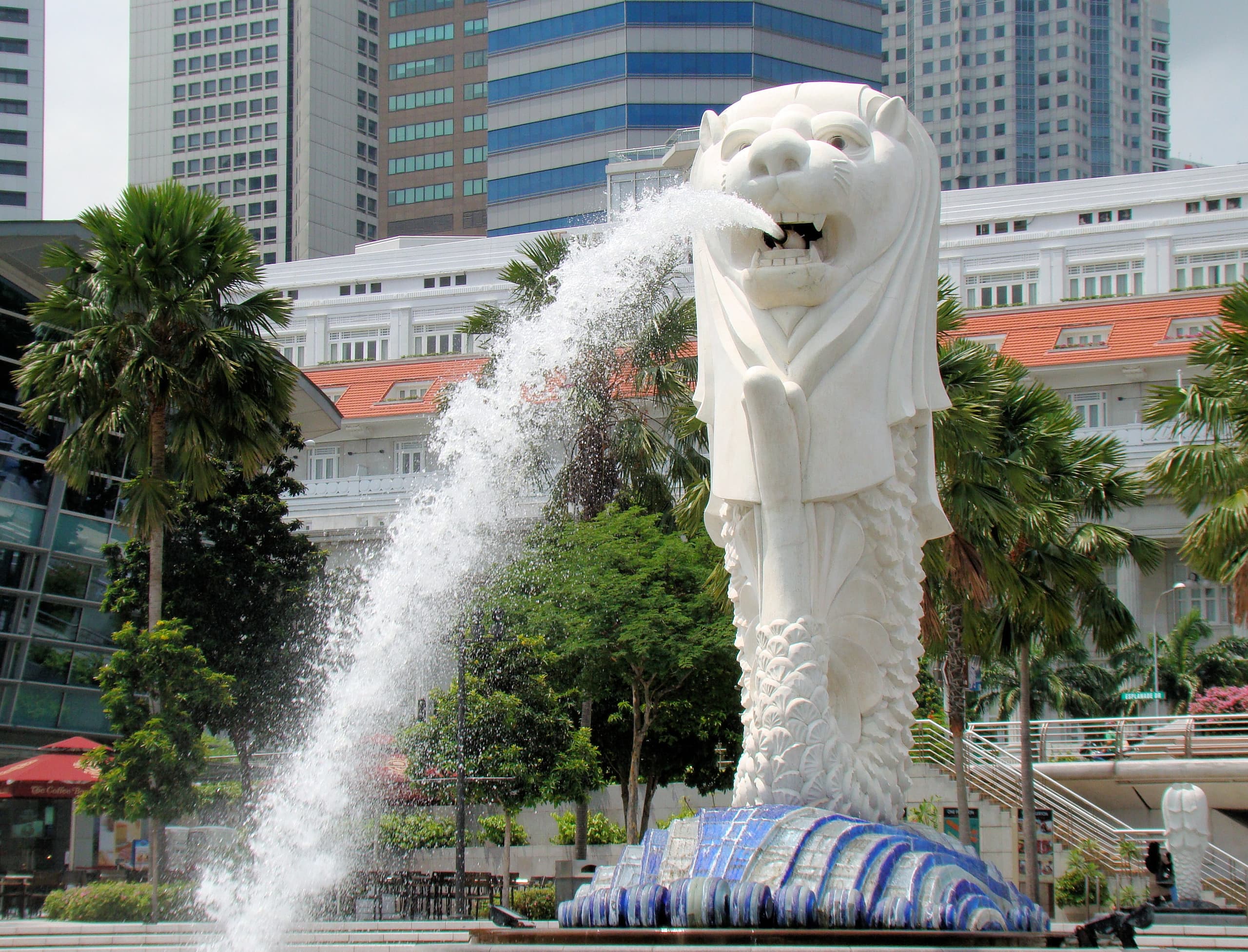 A tall pale statue of a creature with a lion’s head and a fish’s body, mouth open as a fountain, standing upright above a wet base.