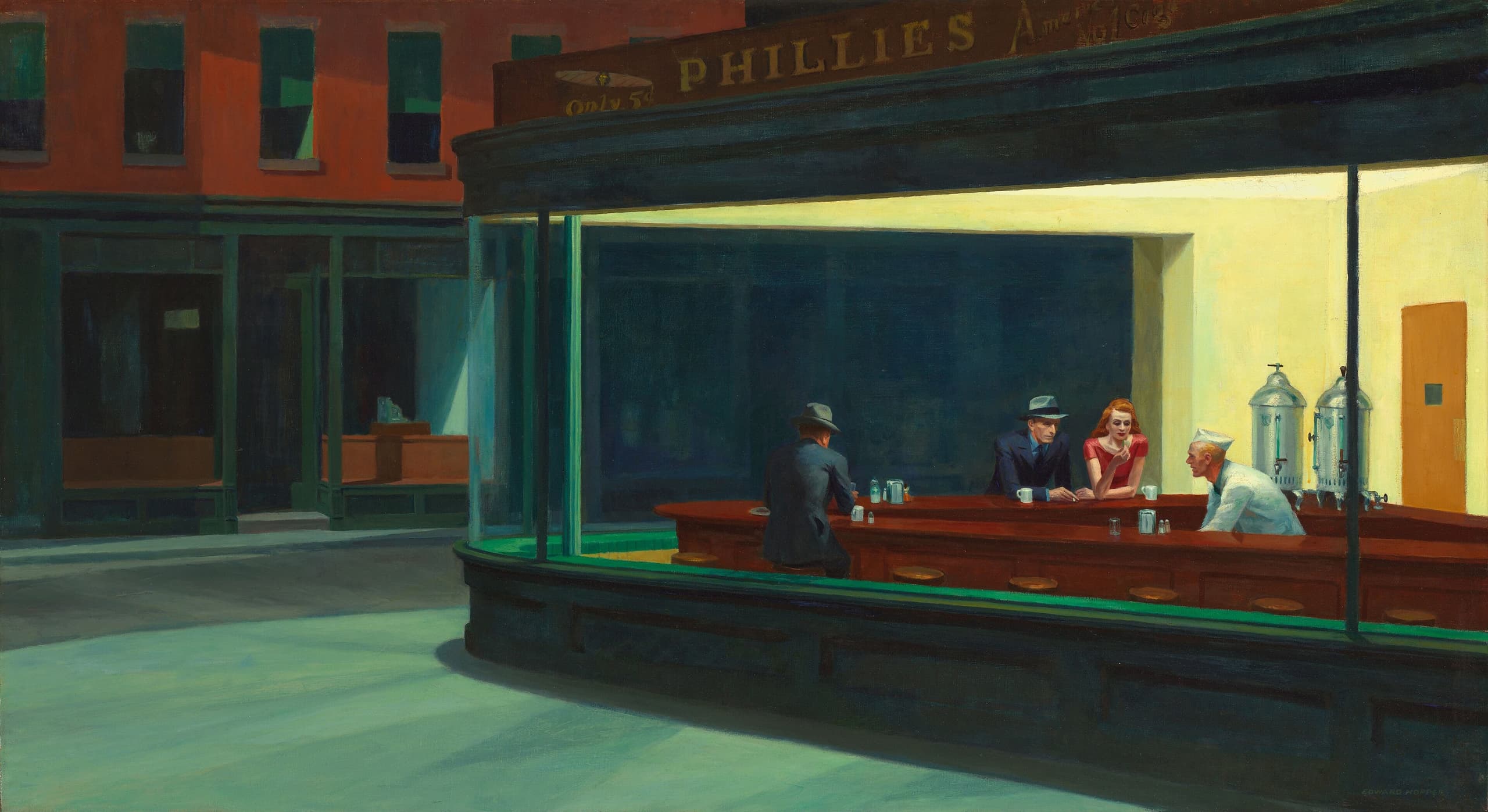 At night, four people sit inside a brightly lit diner seen through a large glass window; the urban street outside is dark and empty.