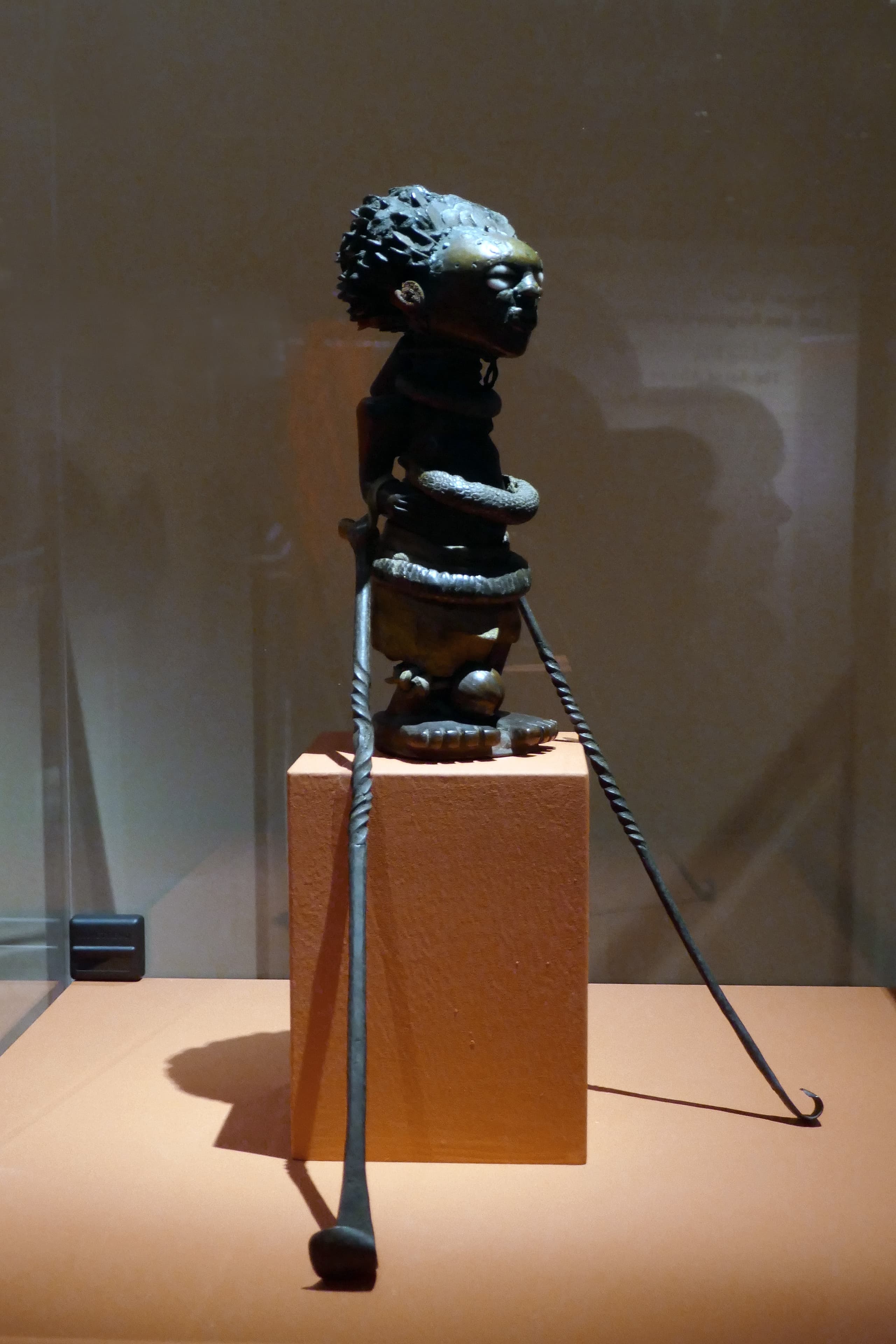 A wooden figure bristling with hundreds of iron nails and blades driven into its surface at all angles. A mass of dark resin is packed into the abdomen. The eyes are inlaid with reflective material.