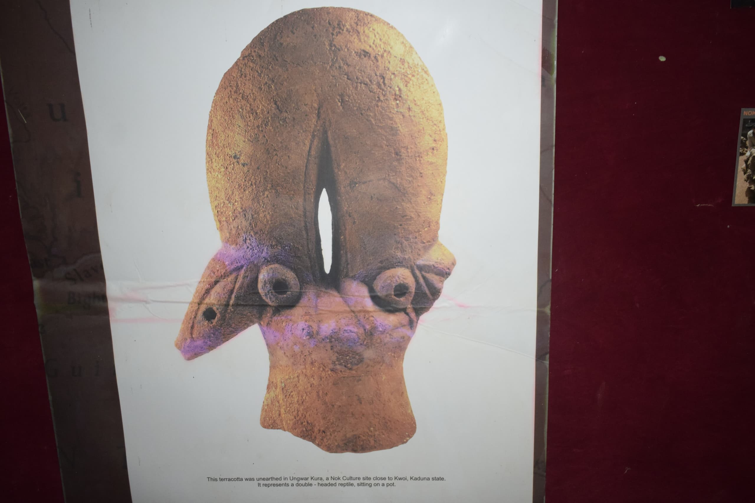 A terracotta head with triangular eyes, drilled pupils, and an elaborate hairstyle carved in relief. The nostrils and ears are perforated.