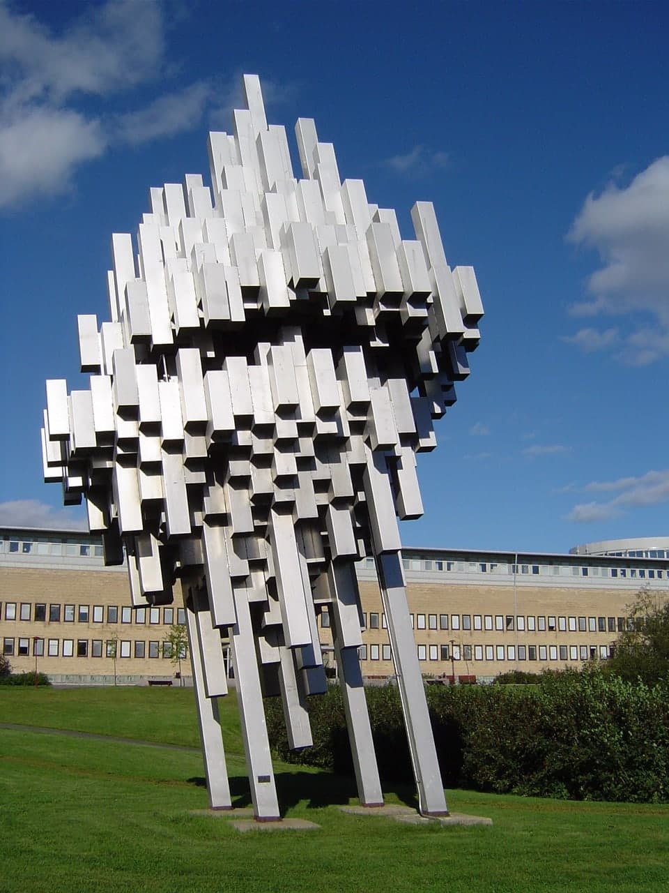 An outdoor stainless-steel sculpture standing on a university campus, open to daylight and weather.