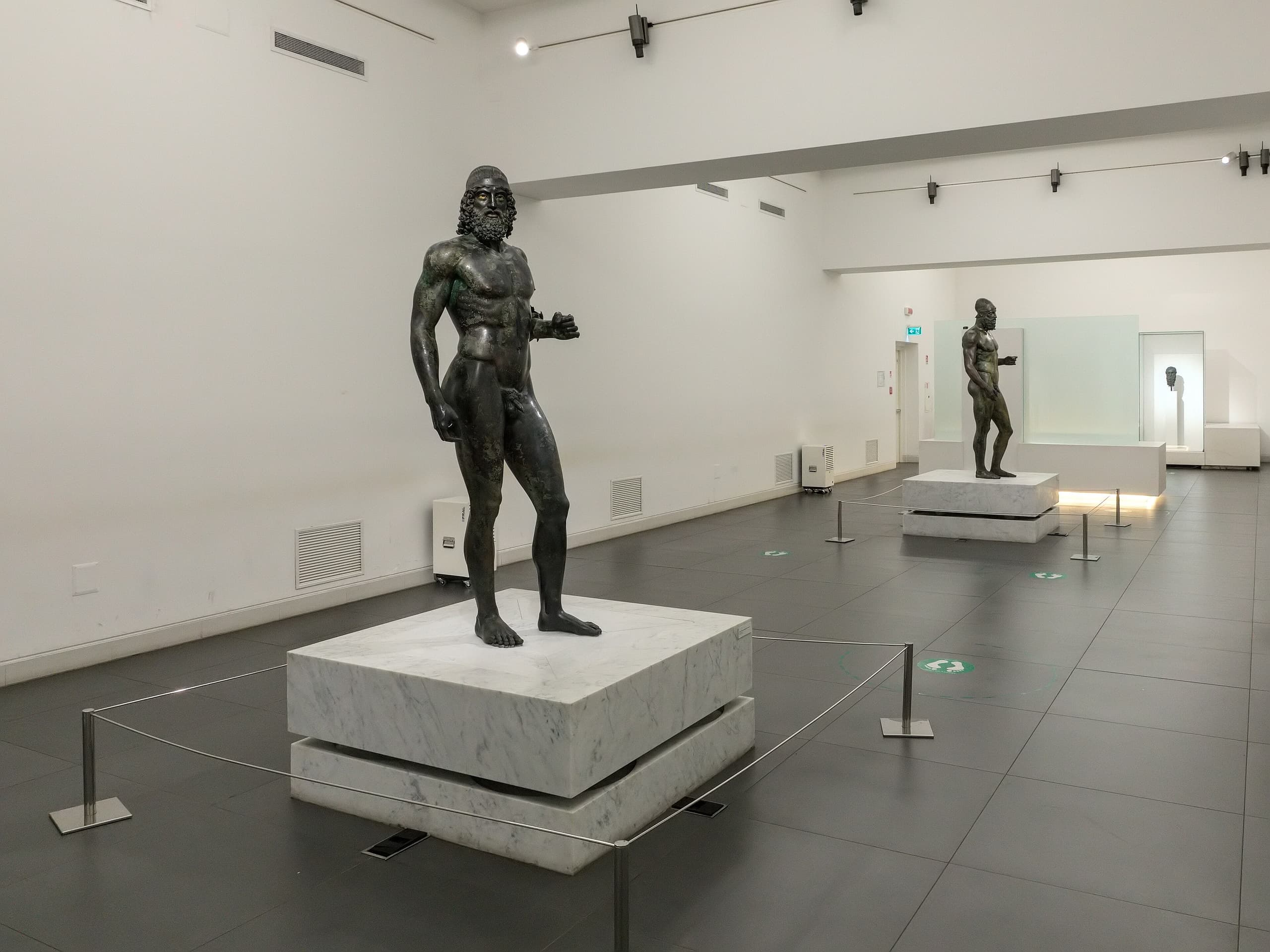 Two standing full-size bronze male warriors, both bearded, one younger in build and one more mature, shown as separate figures.