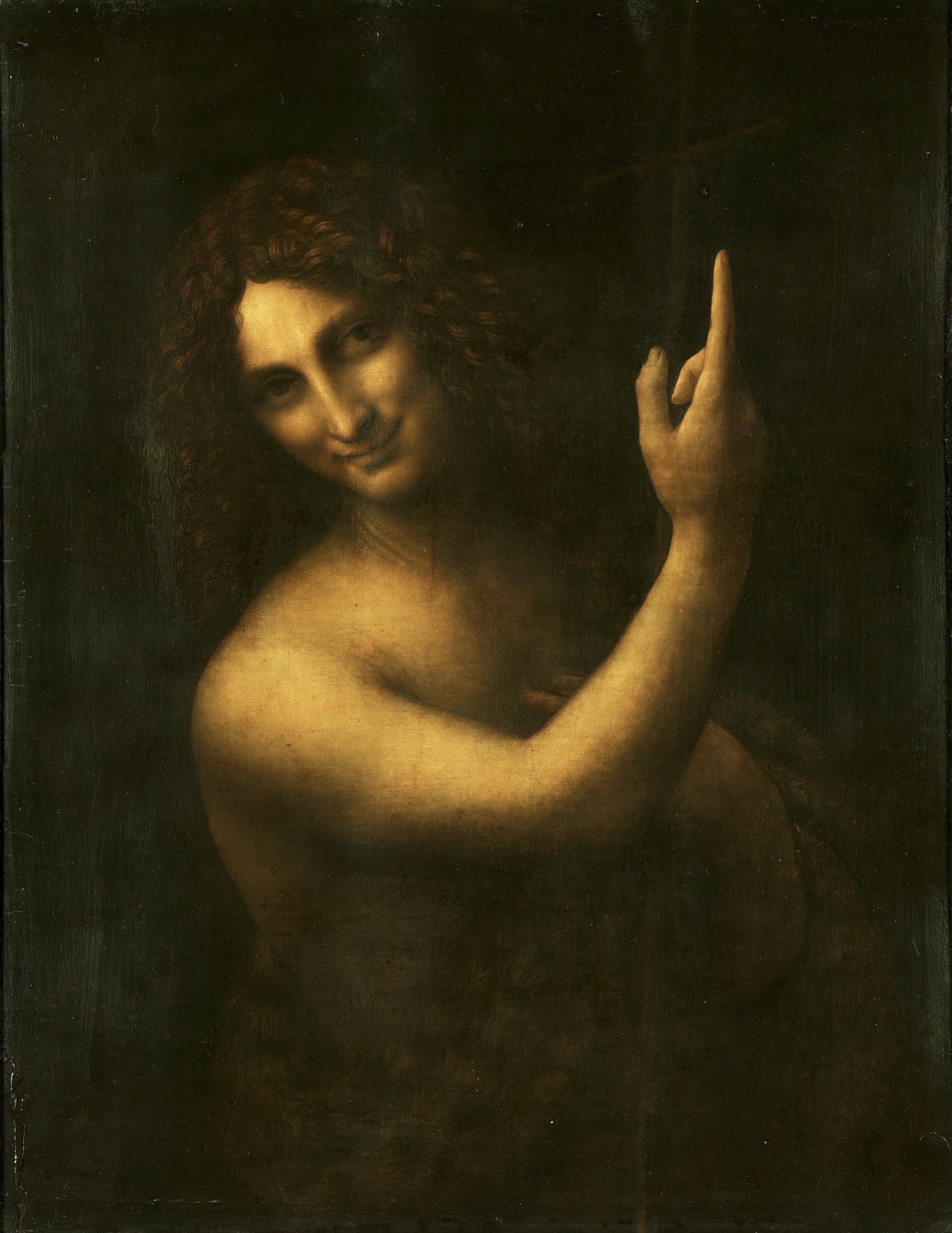 A young man turns from deep shadow toward the viewer, smiling faintly, his right index finger raised above his shoulder while a slender cross rests in his other arm.