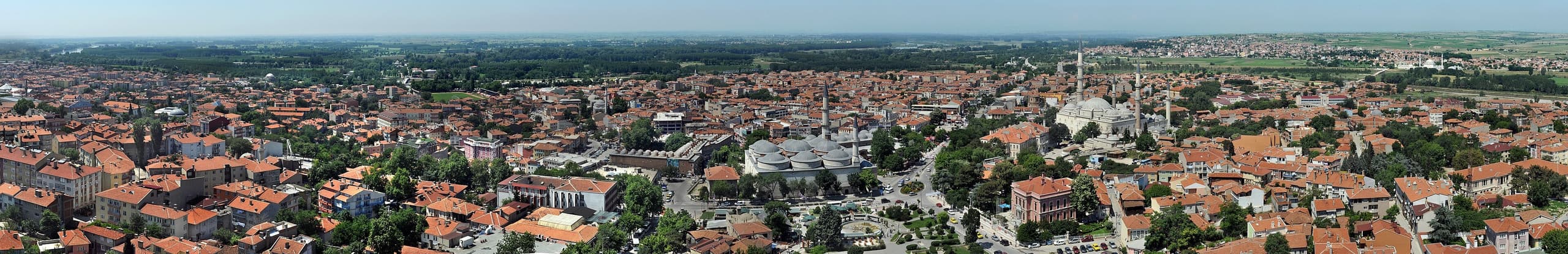 A large domed mosque with four tall slender minarets, one at each corner of the courtyard, rising above a city of low buildings.