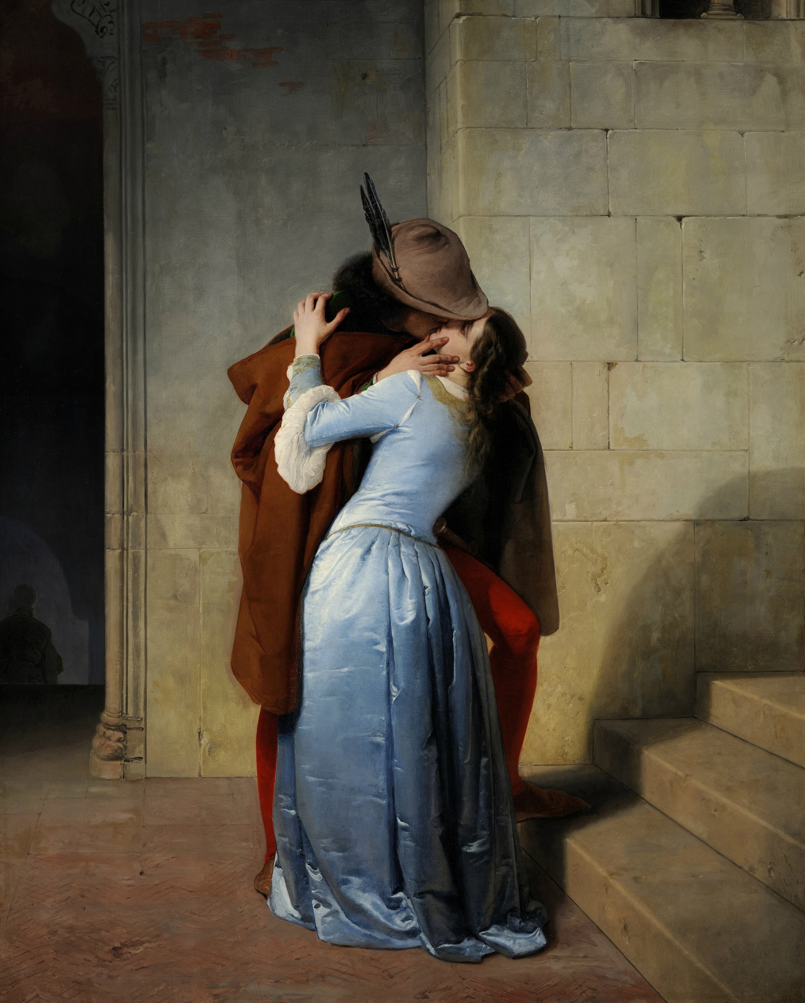 A man in a dark cloak and hat embraces a woman in a pale blue dress on a stone stair; their faces meet in a kiss beneath a shadowed arch.