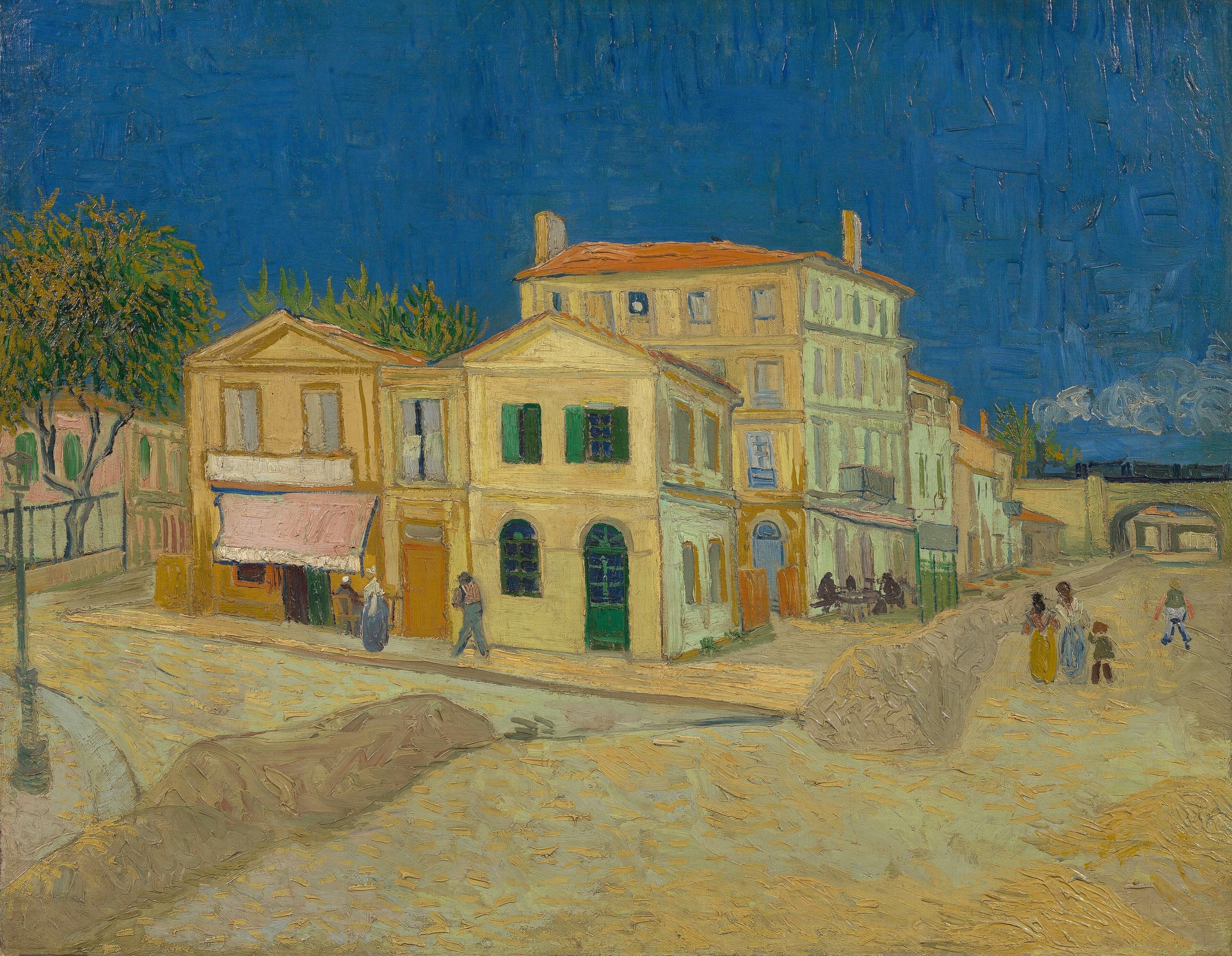 A sunlit street corner in Arles: a yellow two-storey house with green shutters, a pink building to the left, figures on the pavement, and an avenue running right toward railway bridges under a broad blue sky.