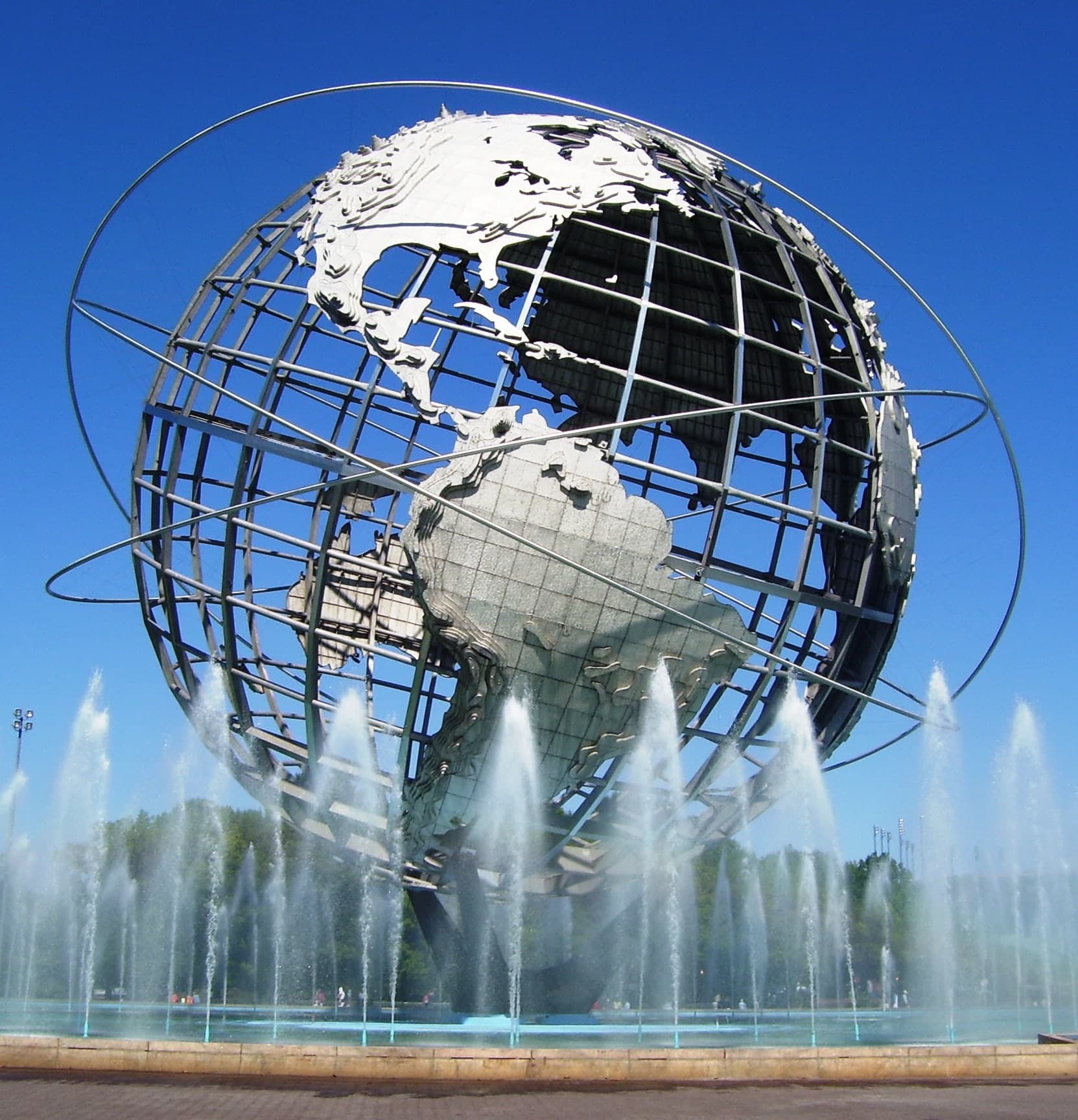 A very large open steel globe on a tripod base, standing in a circular pool. Continents in raised relief are bolted onto a cage of rings running pole to pole and around the equator; the oceans are empty gaps. Three tilted rings encircle the sphere. Jets of water rise around the base.