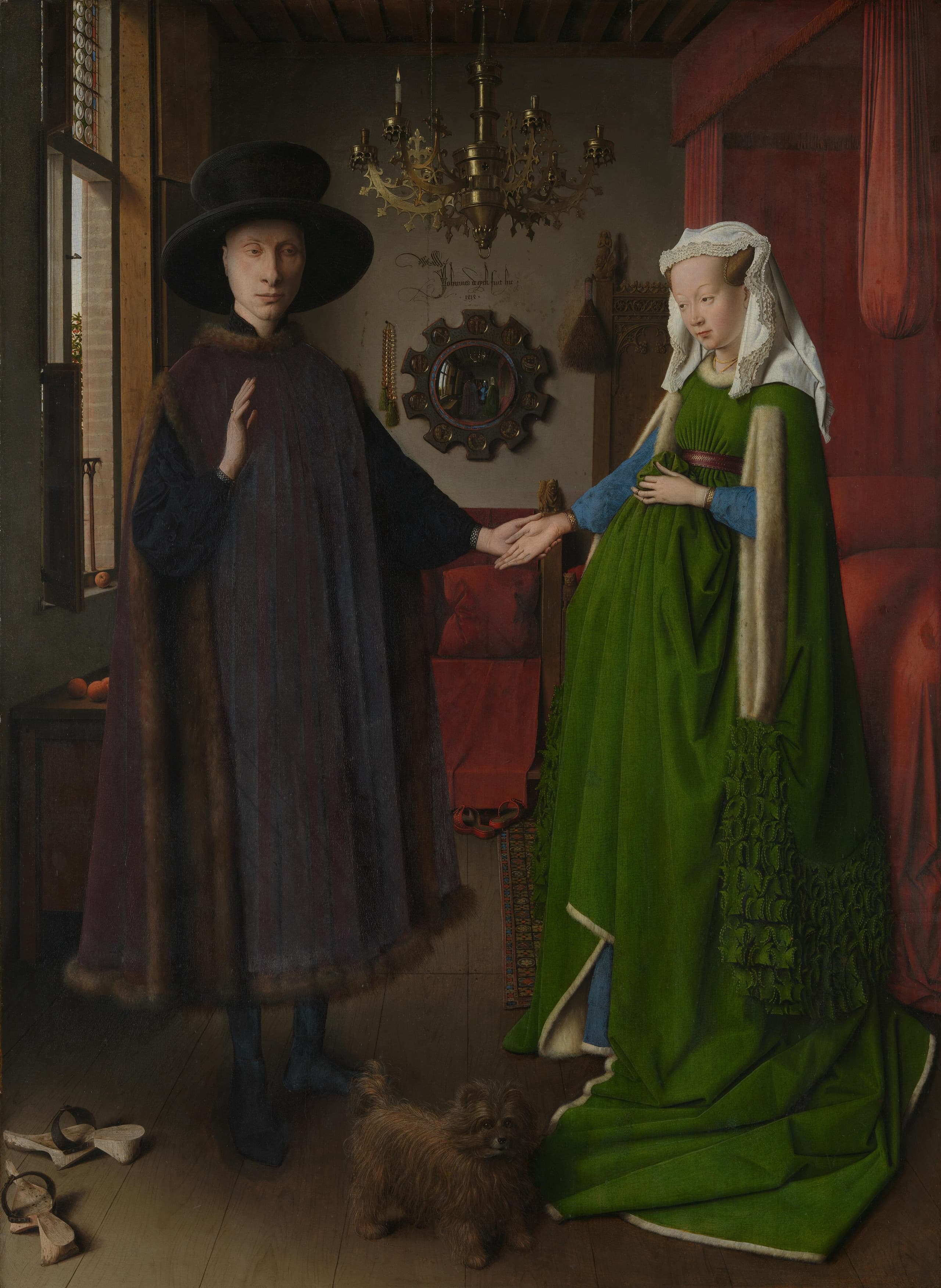 A man in a dark fur-trimmed robe and a woman in a green gown with a long train stand facing each other in a dim interior, a small dog between them. A convex mirror hangs on the back wall, and a brass chandelier with one lit candle hangs from the ceiling.