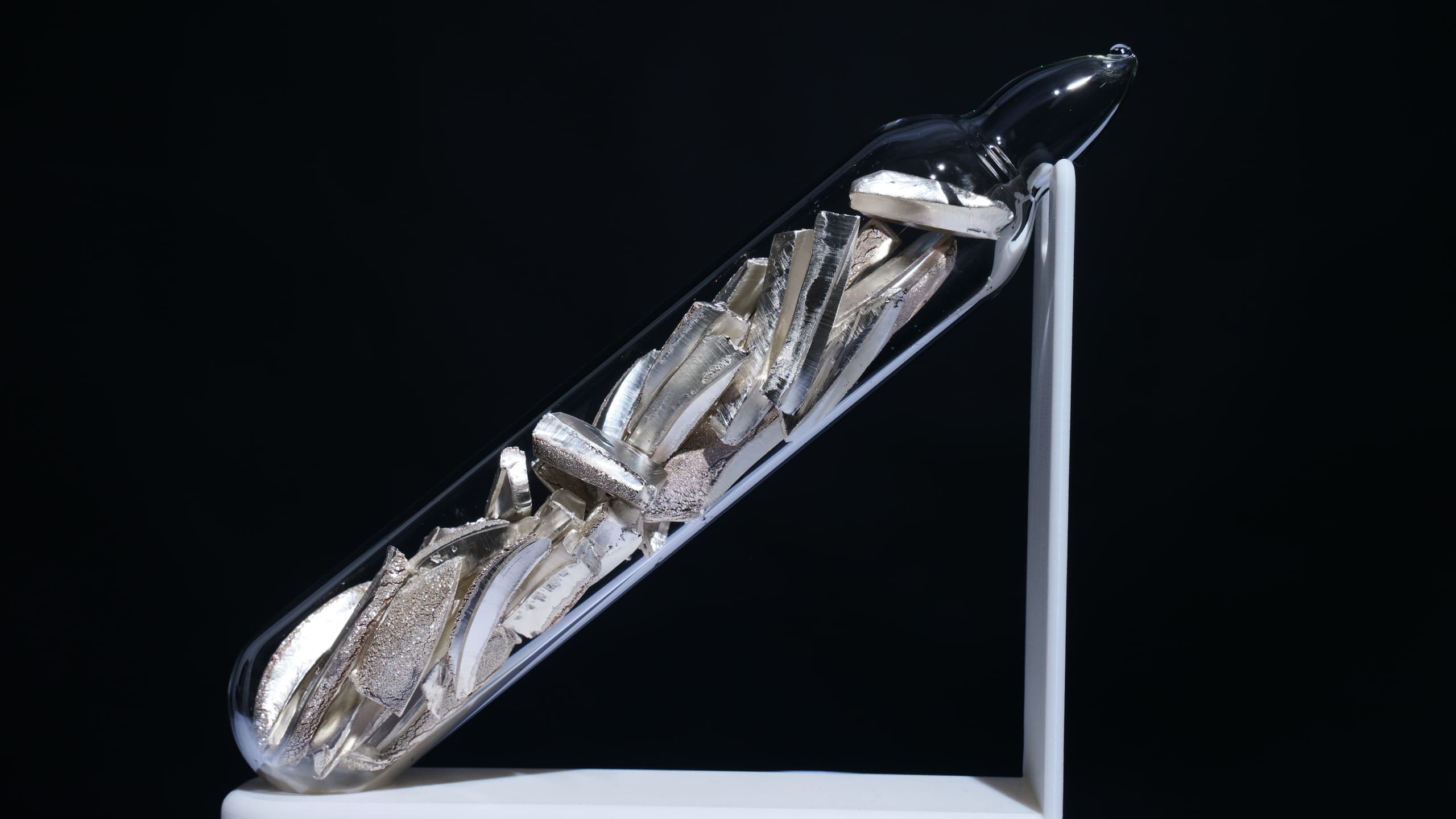 A soft, silvery-white metal with a fresh metallic lustre on a cut surface, shown against a dark background.