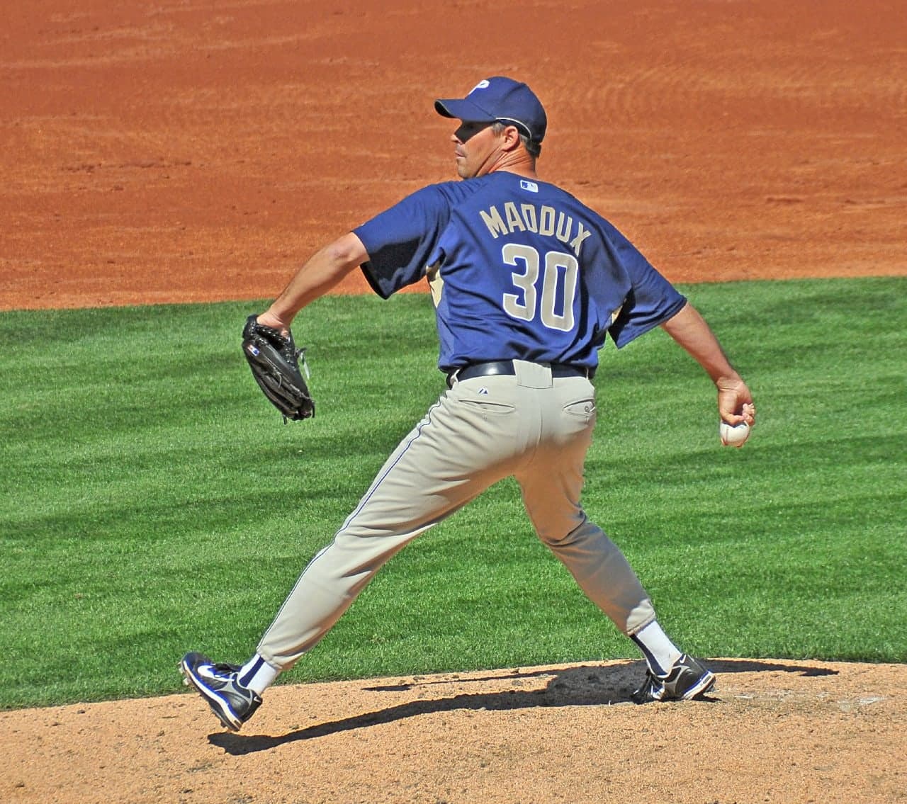 Head-and-shoulders portrait of a man in a white pinstriped baseball uniform with navy piping and a navy cap with a red letter, holding a baseball in his right hand near his chest, looking directly at the camera.