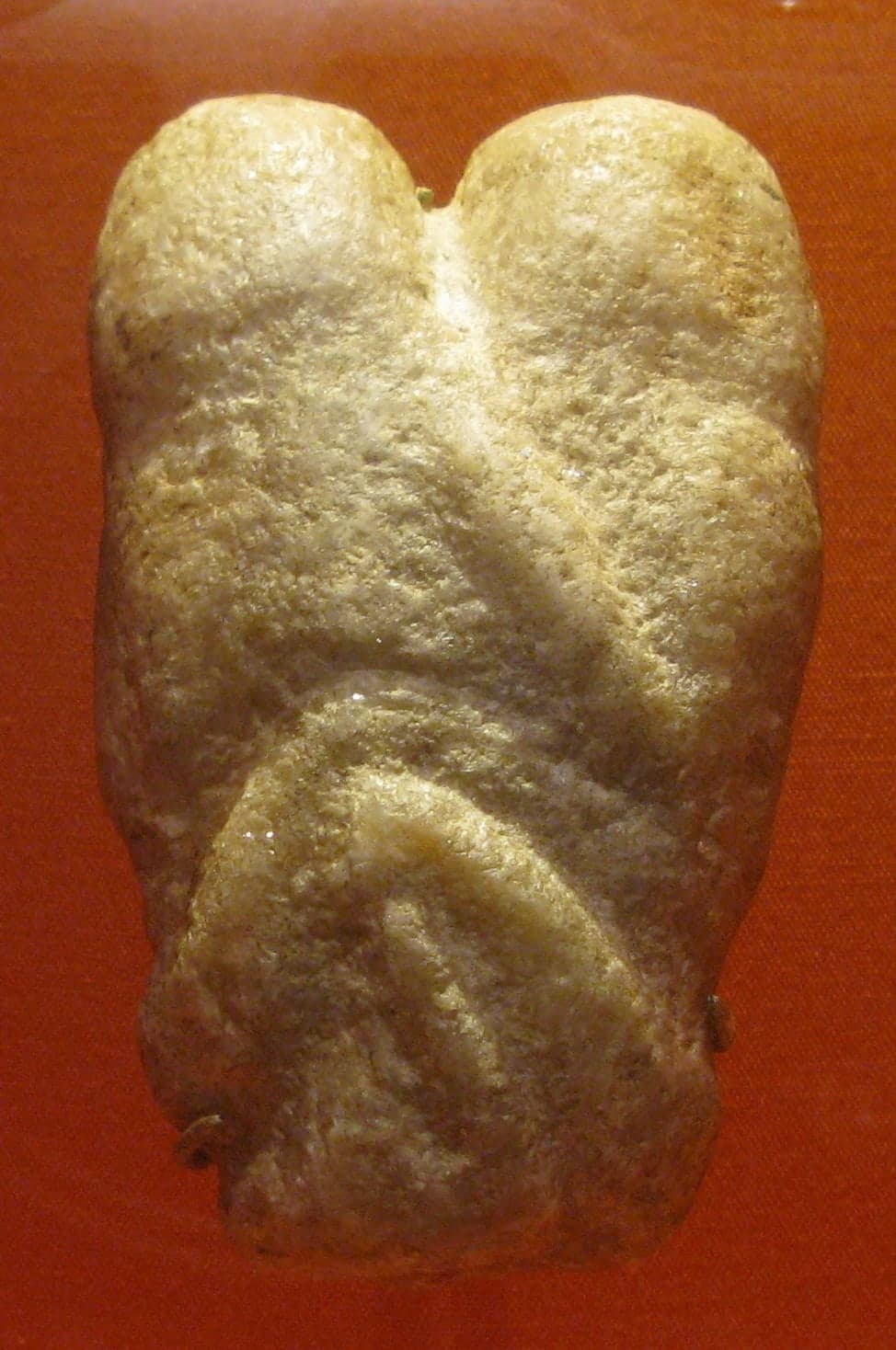 A small, smooth brown calcite sculpture of two abstracted figures embracing, their heads tilted together and their bodies merging into a single rounded form below the shoulders.