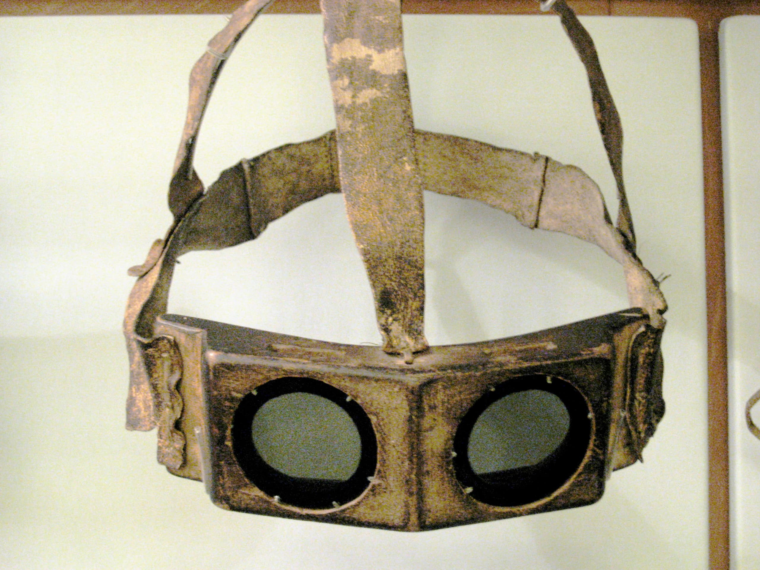 A pair of carved goggles with a smooth, contoured outer surface and narrow horizontal slits for the eyes, held in place by a cord or strap.