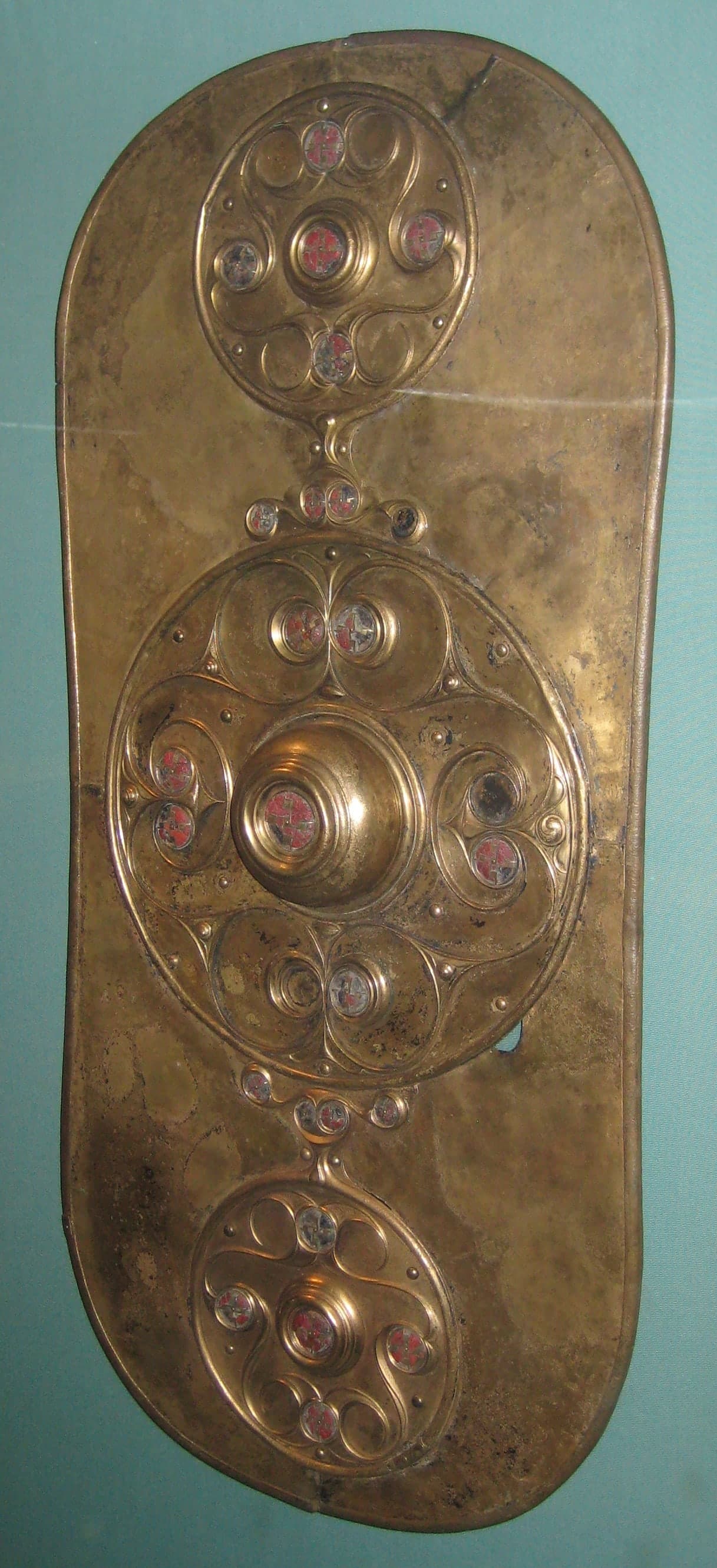 A long, narrow bronze sheet with three large circular decorations arranged vertically, each filled with raised spirals and smaller roundels, the metal surface dark with age and patina.