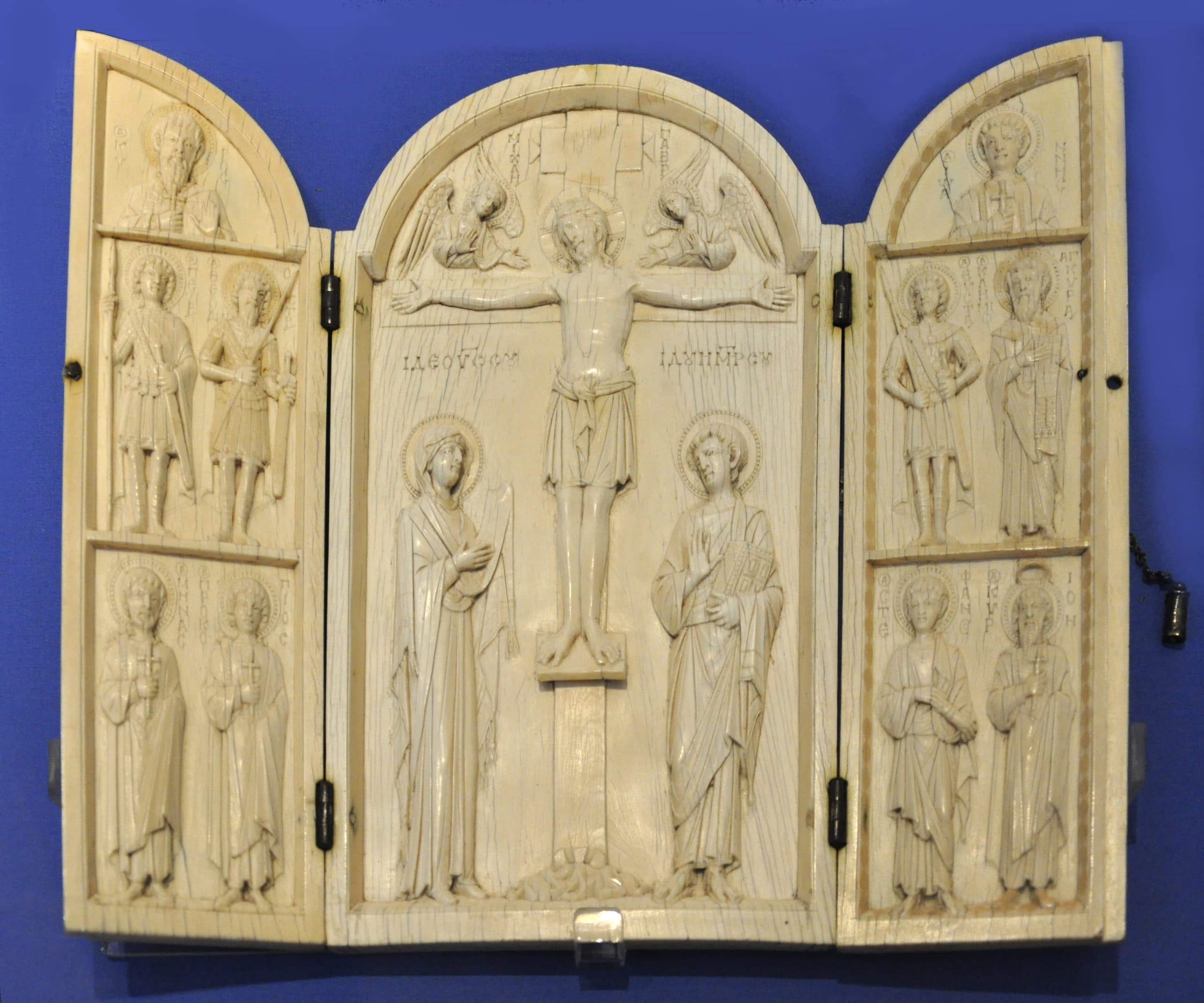A small ivory panel with two narrower hinged wings, opened out; the pale carved surfaces are crowded with standing figures in fine drapery, framed by narrow borders.