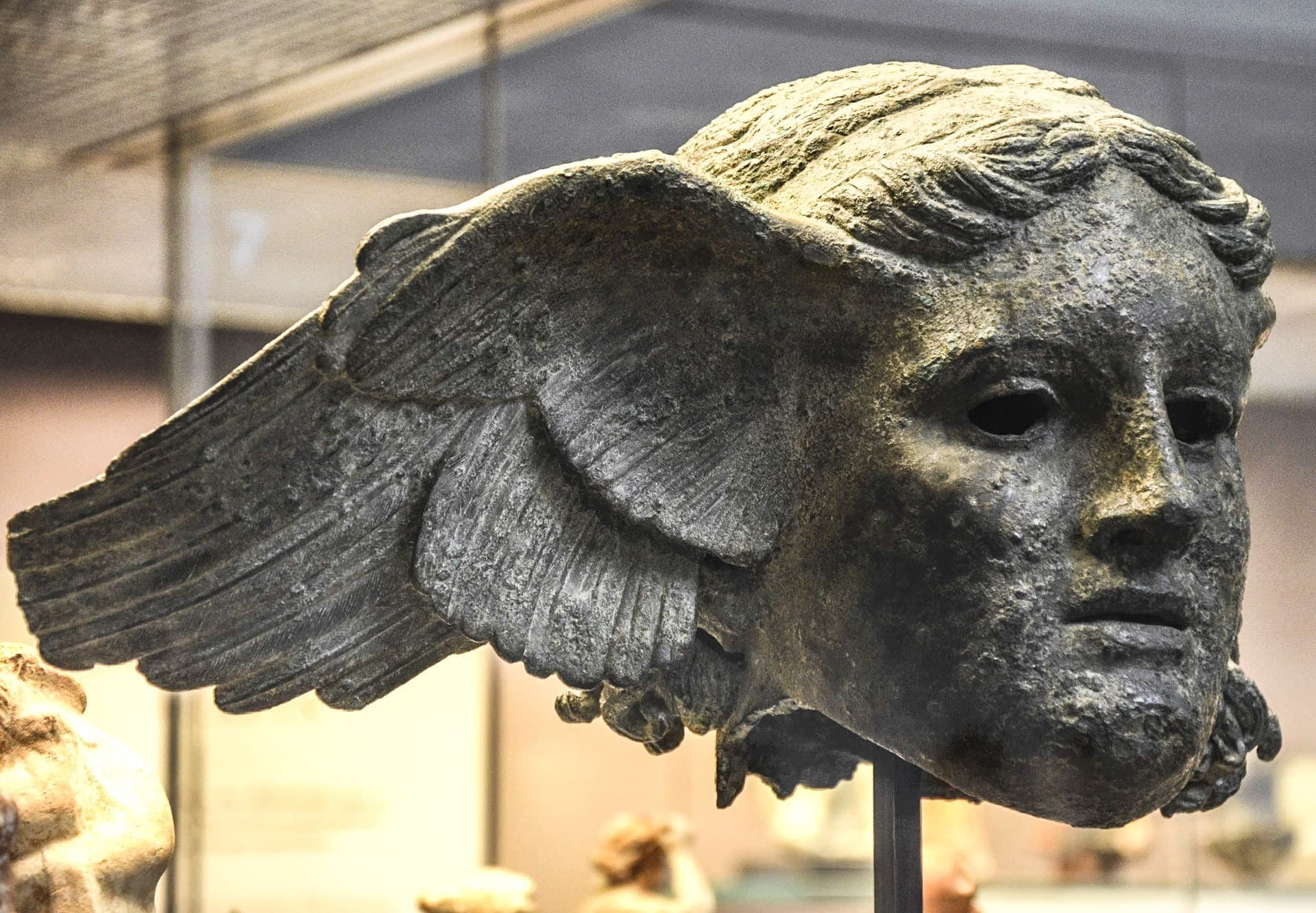 A bronze sculpture of a bearded man with closed eyes and hair falling over his forehead. The features are worn and there is no nose; this may be because it was deliberately removed.