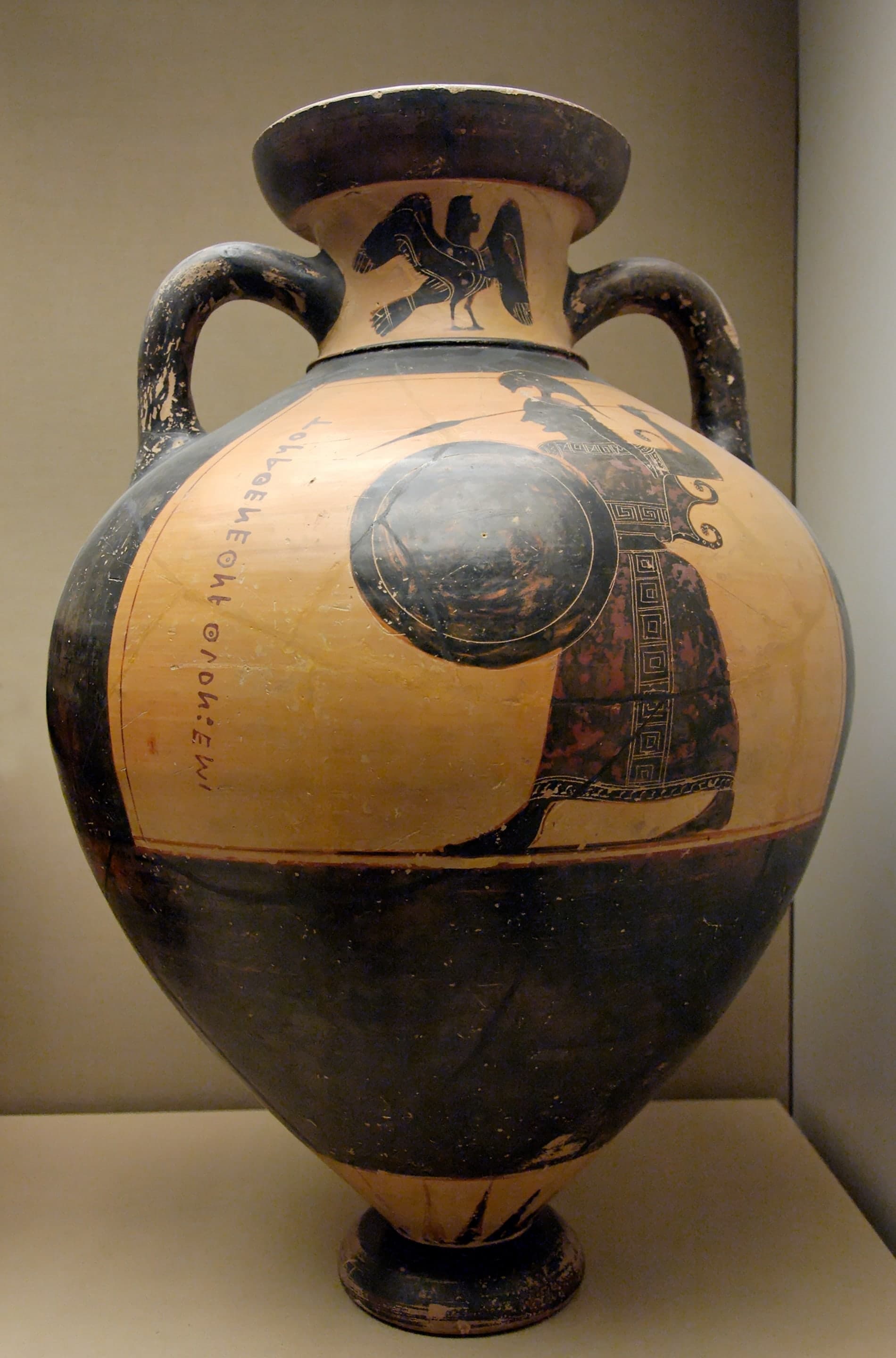 A short, squat black-figure amphora with a low mouth, short neck, small handles close to the body, and a tiny foot; one side incomplete where the surface was damaged.