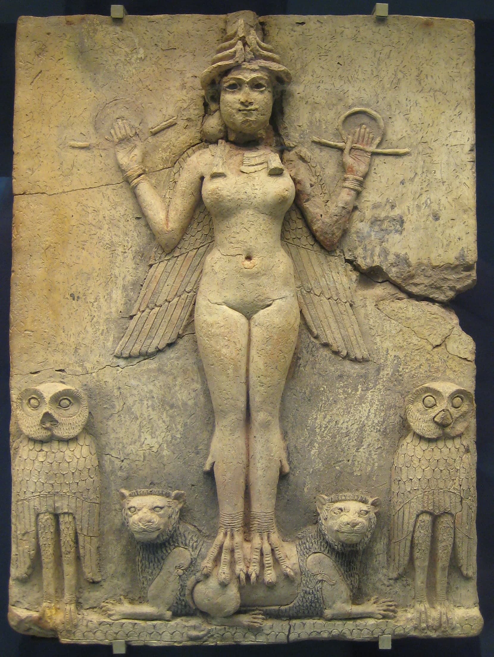 A terracotta relief of a nude winged female figure with bird talons, wearing a horned crown, holding rod and ring symbols, flanked by two owls and standing on two lions.
