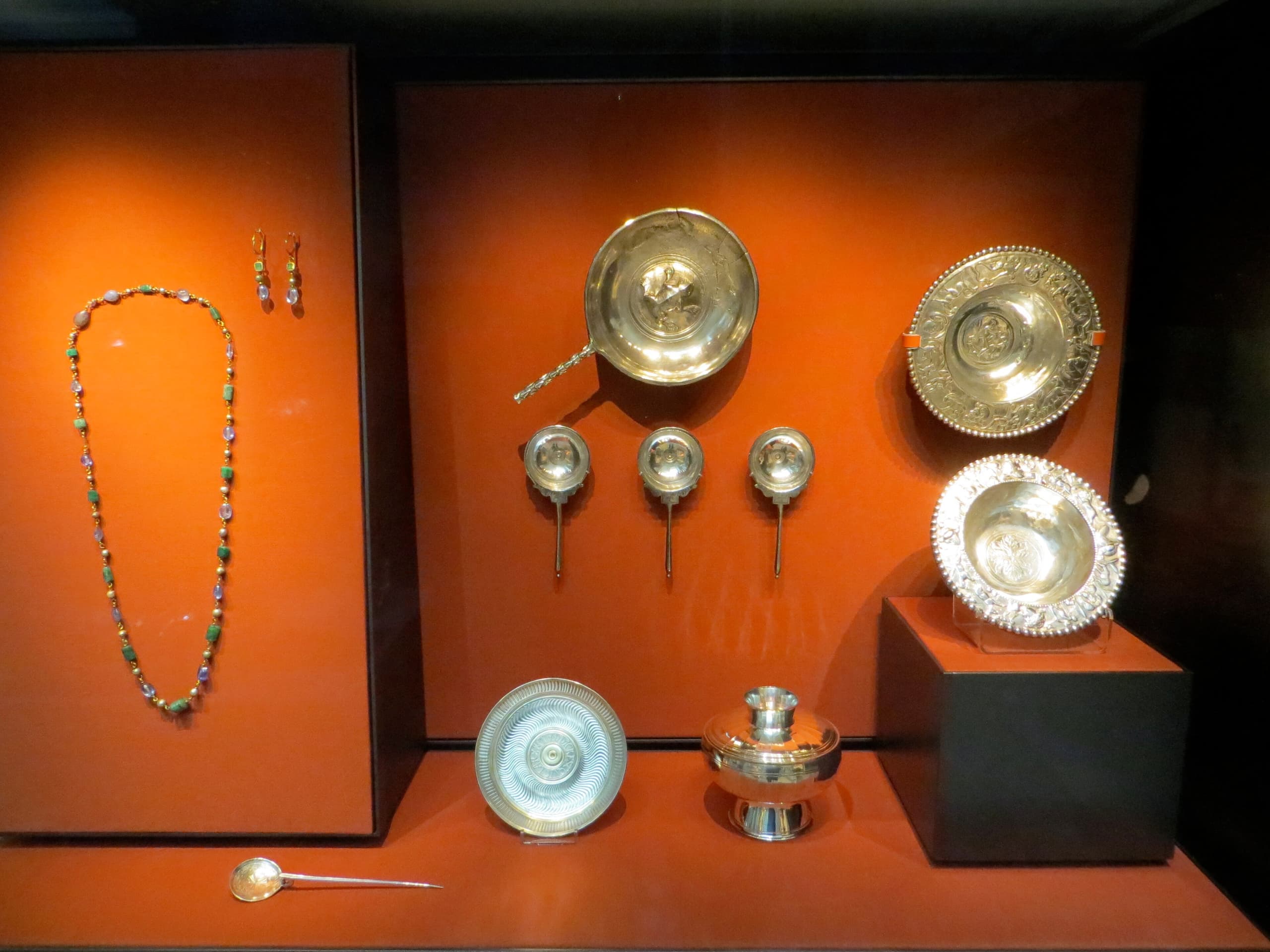 A collection of Roman silver objects including plates, vessels and items of jewellery, arranged on a dark background.