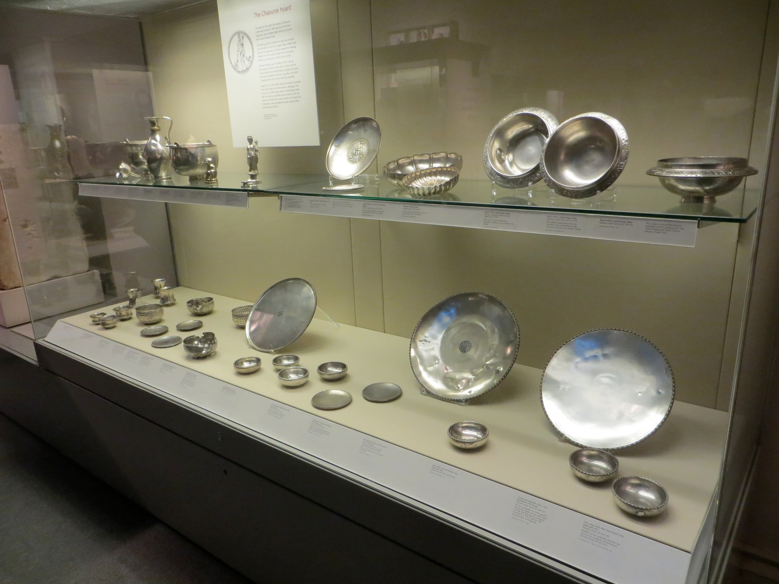A group of Roman silver and bronze table vessels and utensils arranged together, their surfaces muted grey and brown, forming a dense dining assemblage rather than a single showpiece.