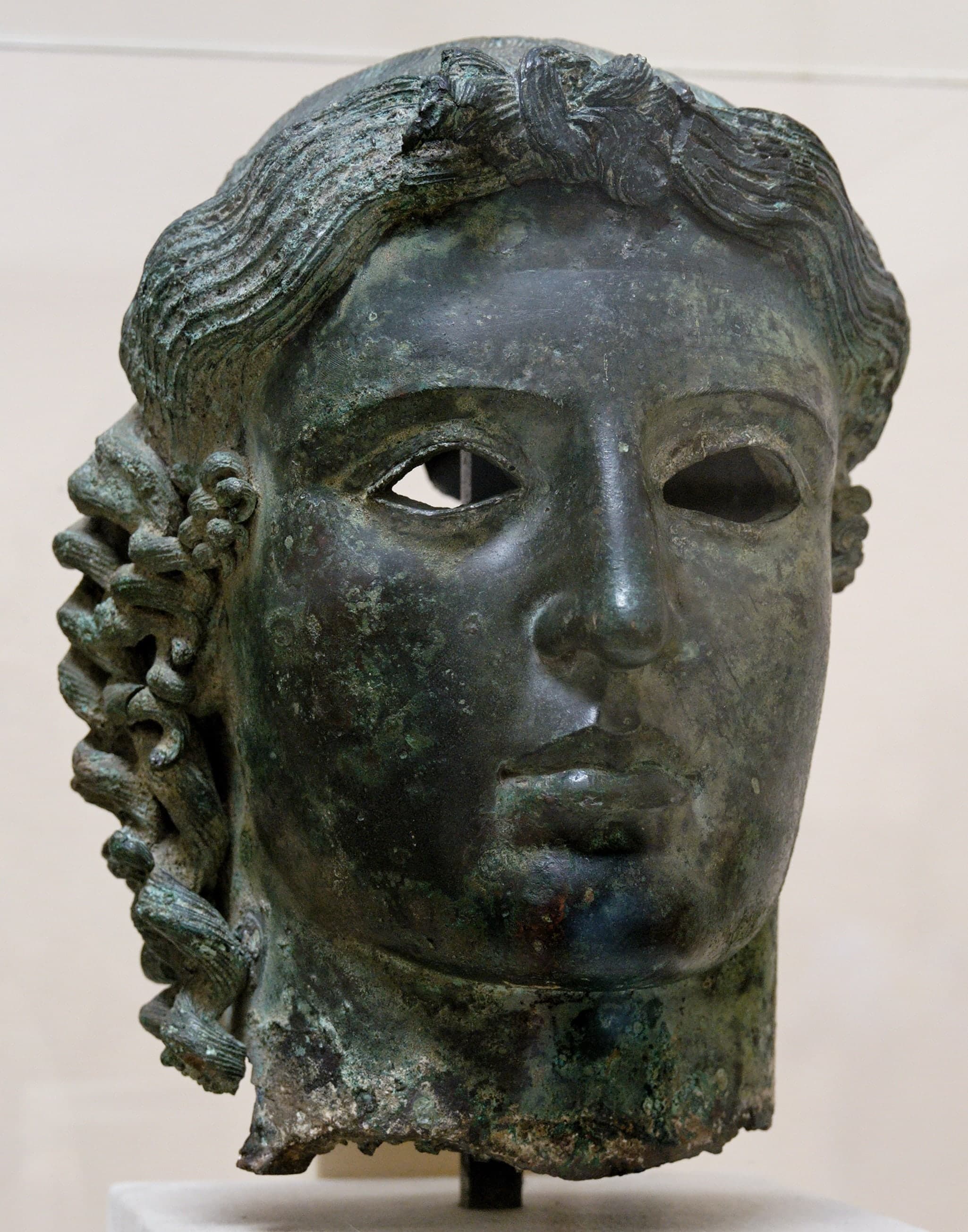 A bronze sculpted head shown in isolation, dark metal surface, broken or truncated at the neck, presented as a museum fragment rather than a full standing figure.