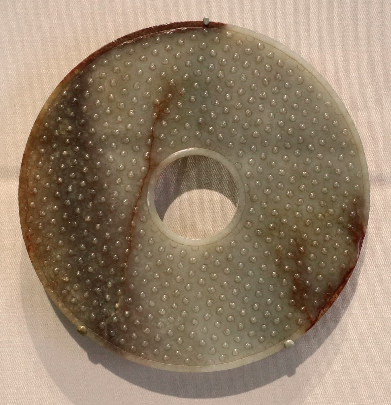 A circular disc of pale green nephrite jade with a central hole, polished smooth, showing subtle variations in translucency across its surface.