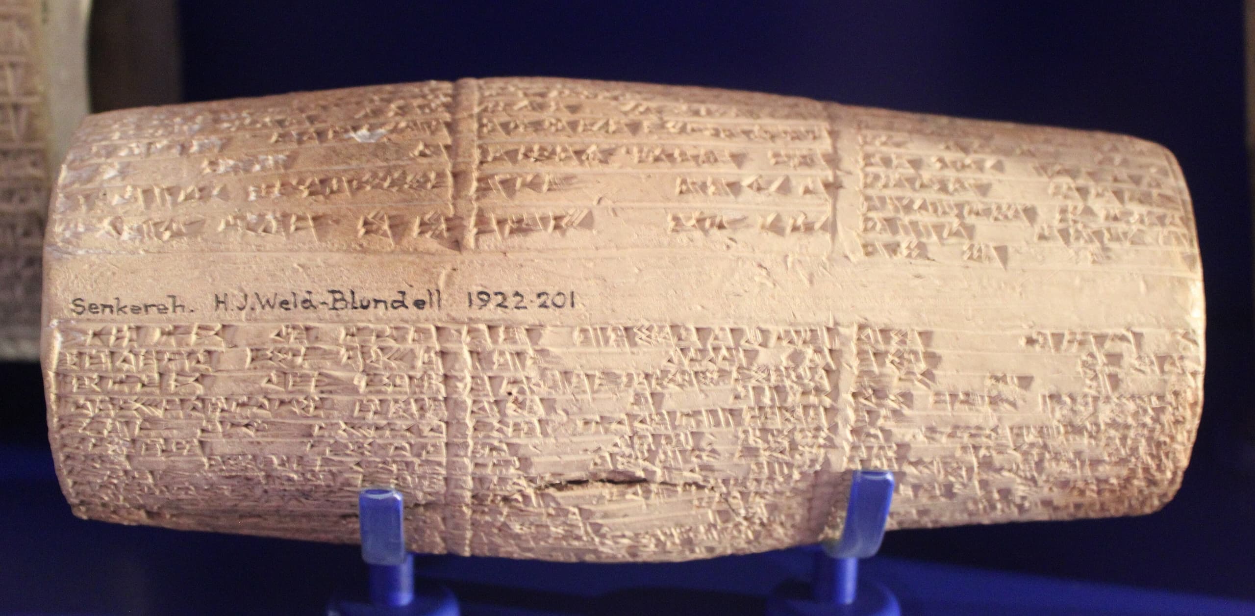 A cylindrical clay object with intricate cuneiform writing covering its surface. The text is arranged in neat rows that wrap around the cylinder from top to bottom.