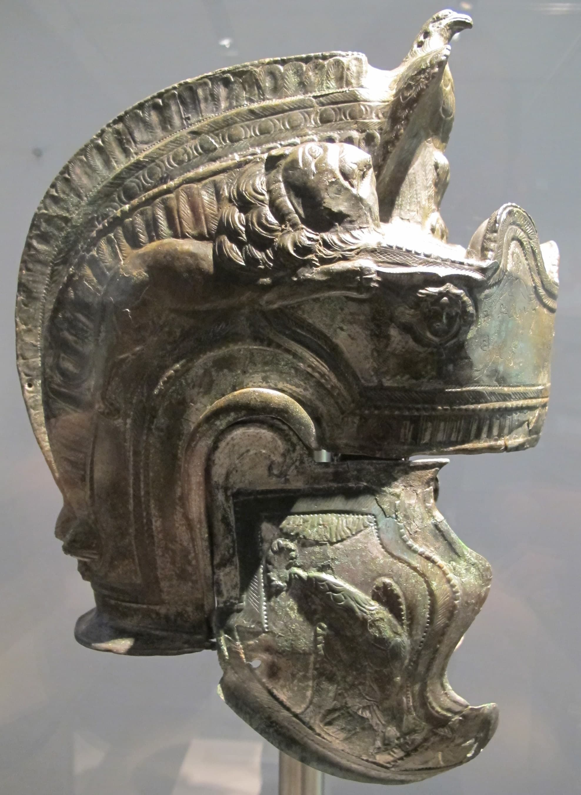 A restored bronze Roman cavalry helmet with ear guards, attachment holes where cheek-pieces once hung, and a surface worked with incised, punched and embossed decoration.