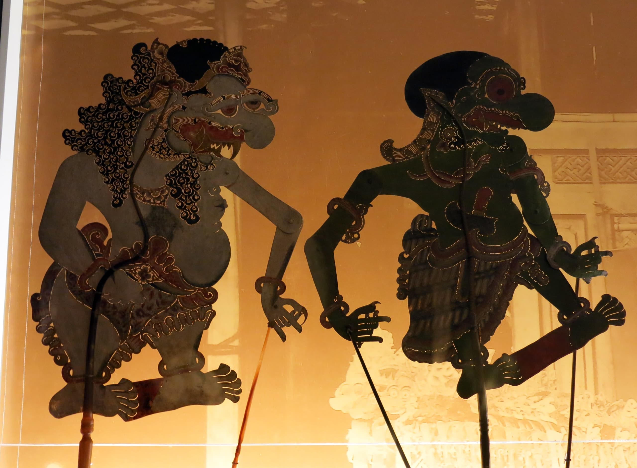 A flat puppet carved from buffalo hide in strict profile, with exaggerated features, elongated limbs, and intricate perforations across the torso and clothing, mounted on a slender rod.