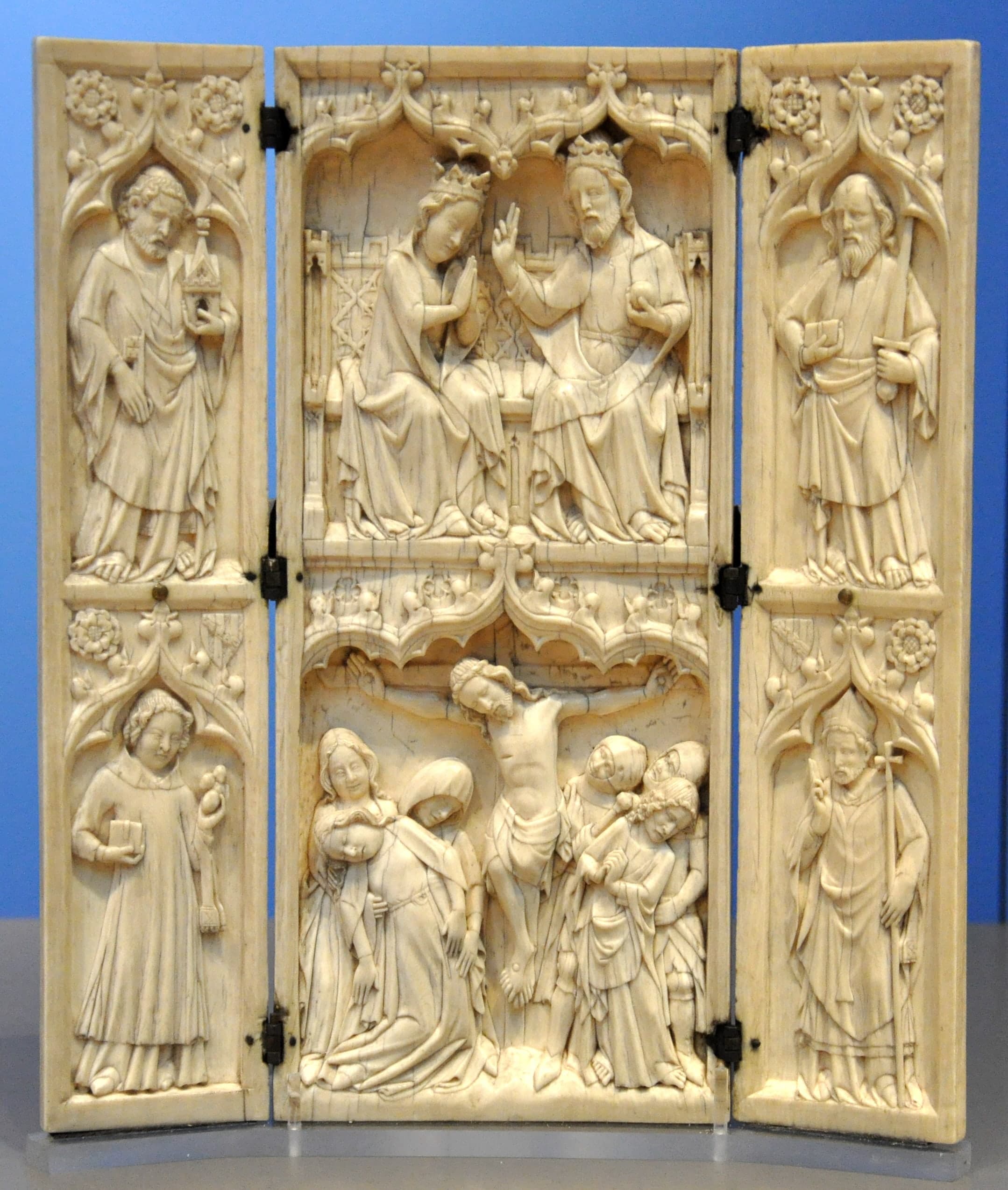 Three hinged panels of pale carved ivory forming a small triptych, the side leaves set to close over the centre, shown as a compact portable object.