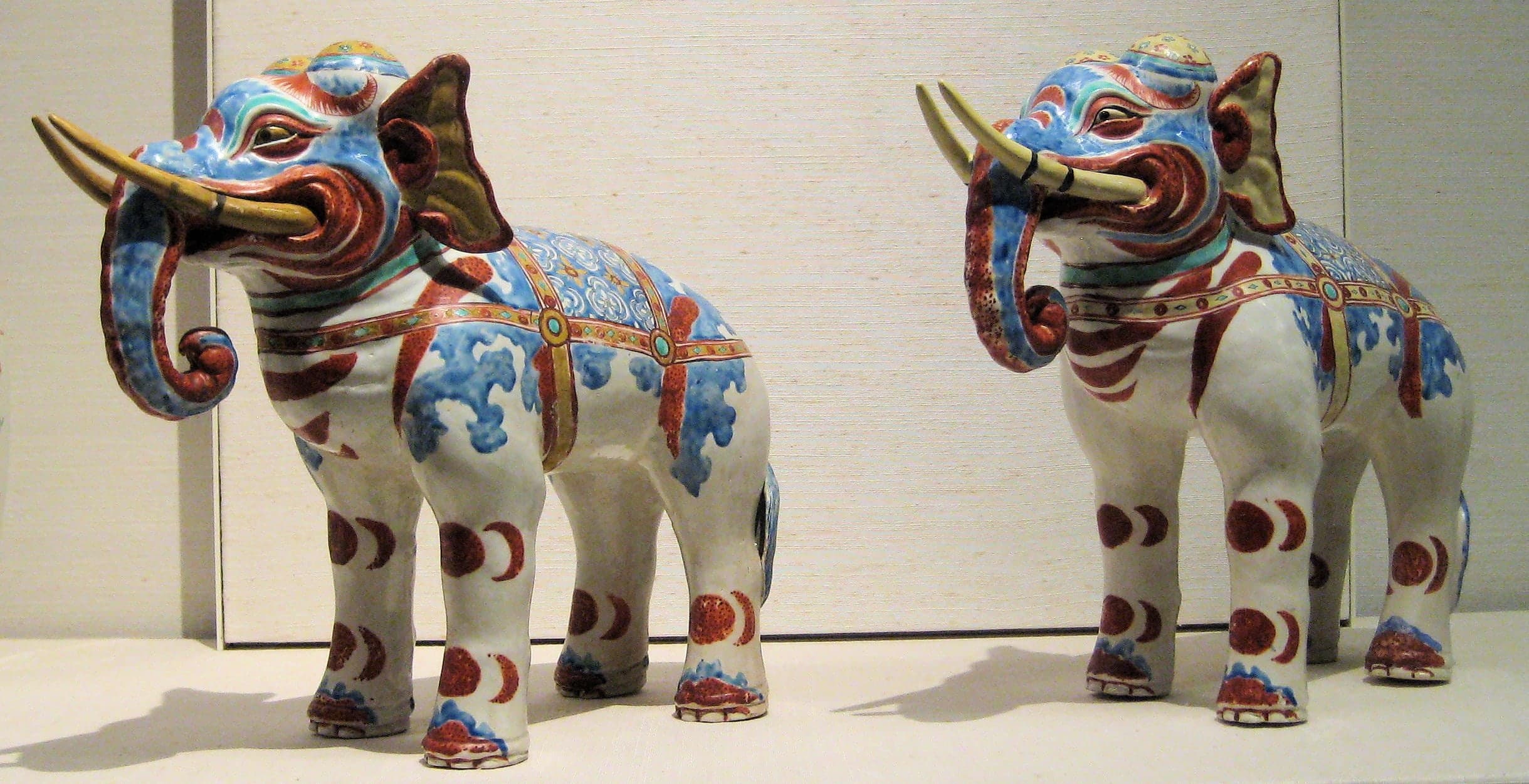 A pair of white porcelain elephants with sparse overglaze colour, standing side by side, compact bodies and curved trunks modelled in a simplified, non-naturalistic manner.