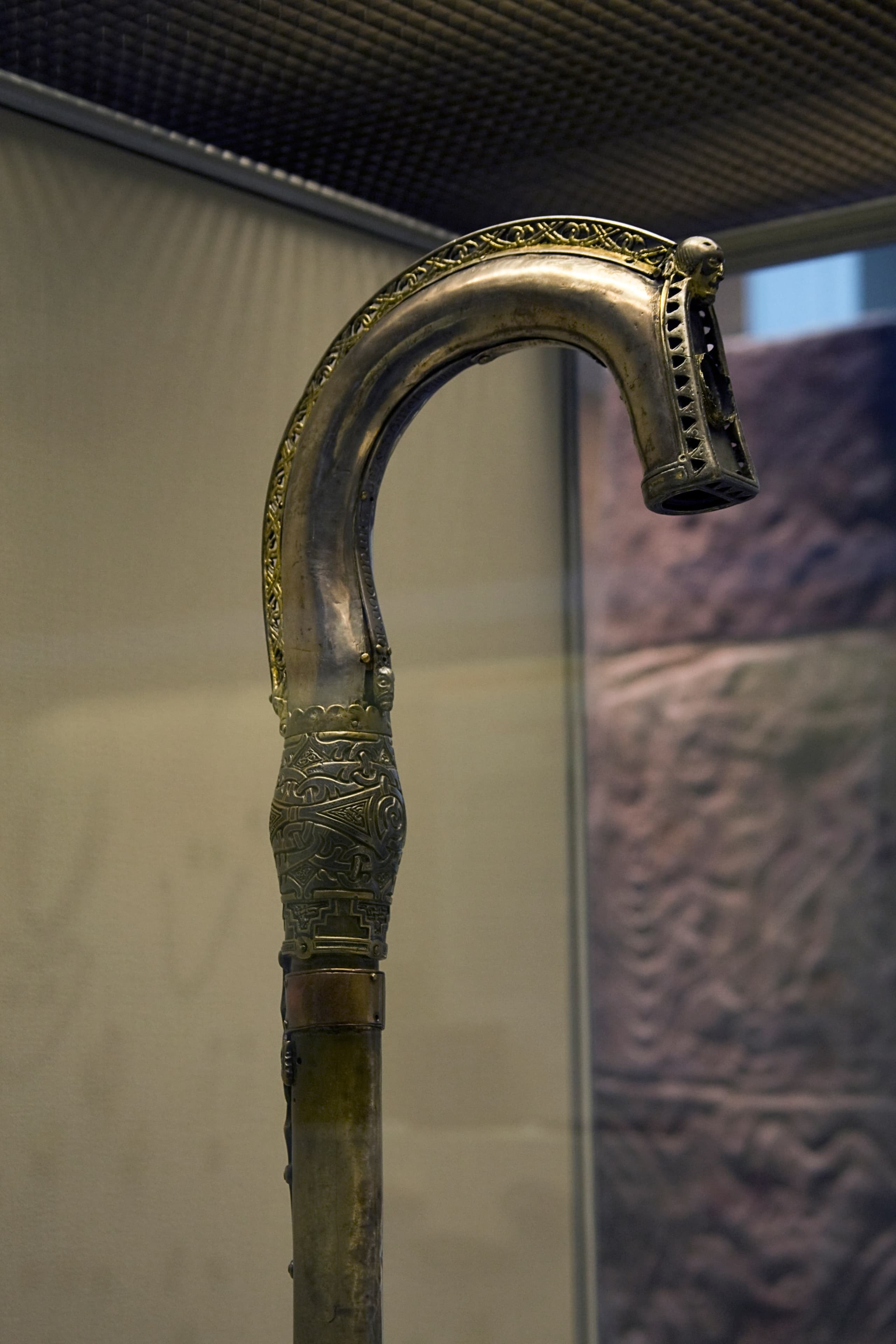 A complete early medieval crozier with a curved head, shown as a tall staff whose surface ornament is in places worn or damaged.