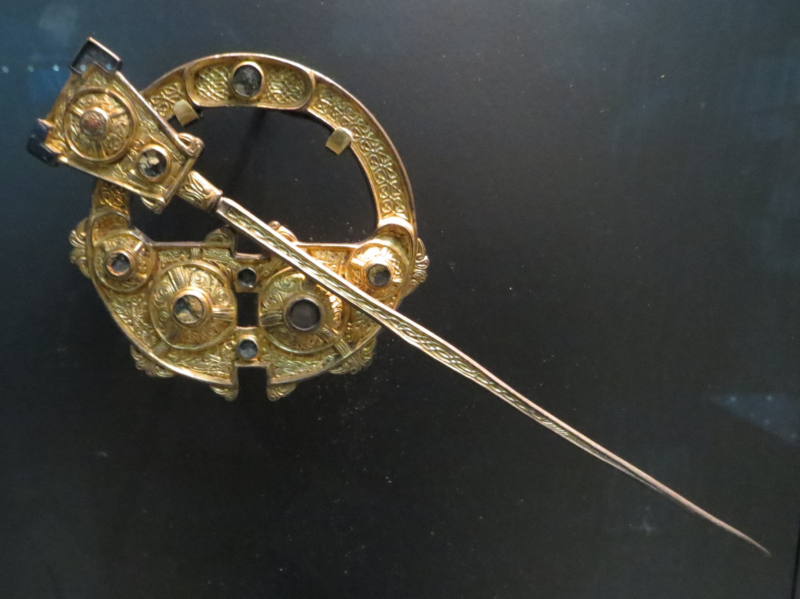 A silver and silver-gilt penannular brooch with a ring, ornate terminals, and a long pin, shown as a freestanding dress fastener.