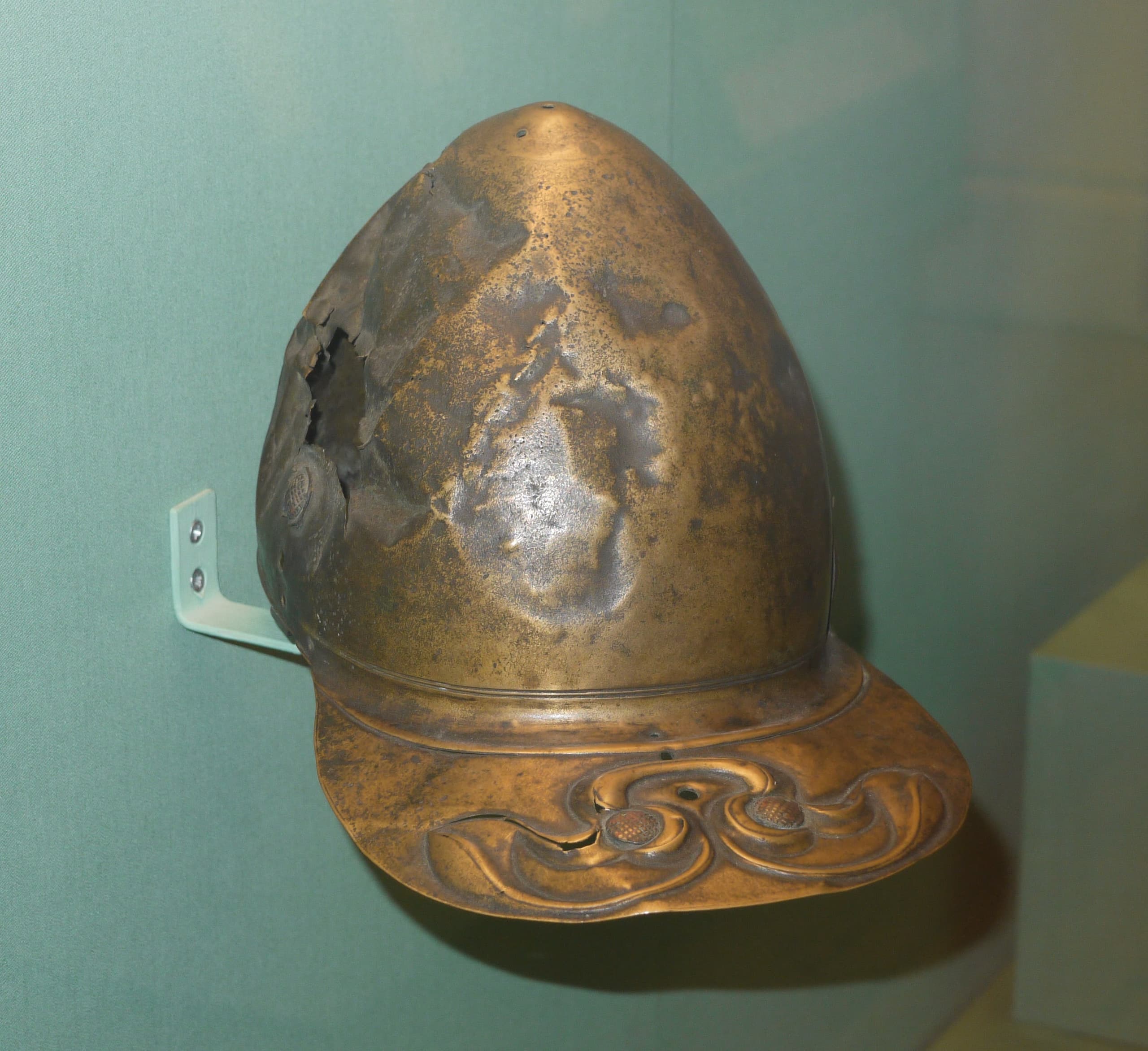 The image shows a helmet made of bronze; the supplied image information gives no reliable detail about its outline, decoration, or condition.