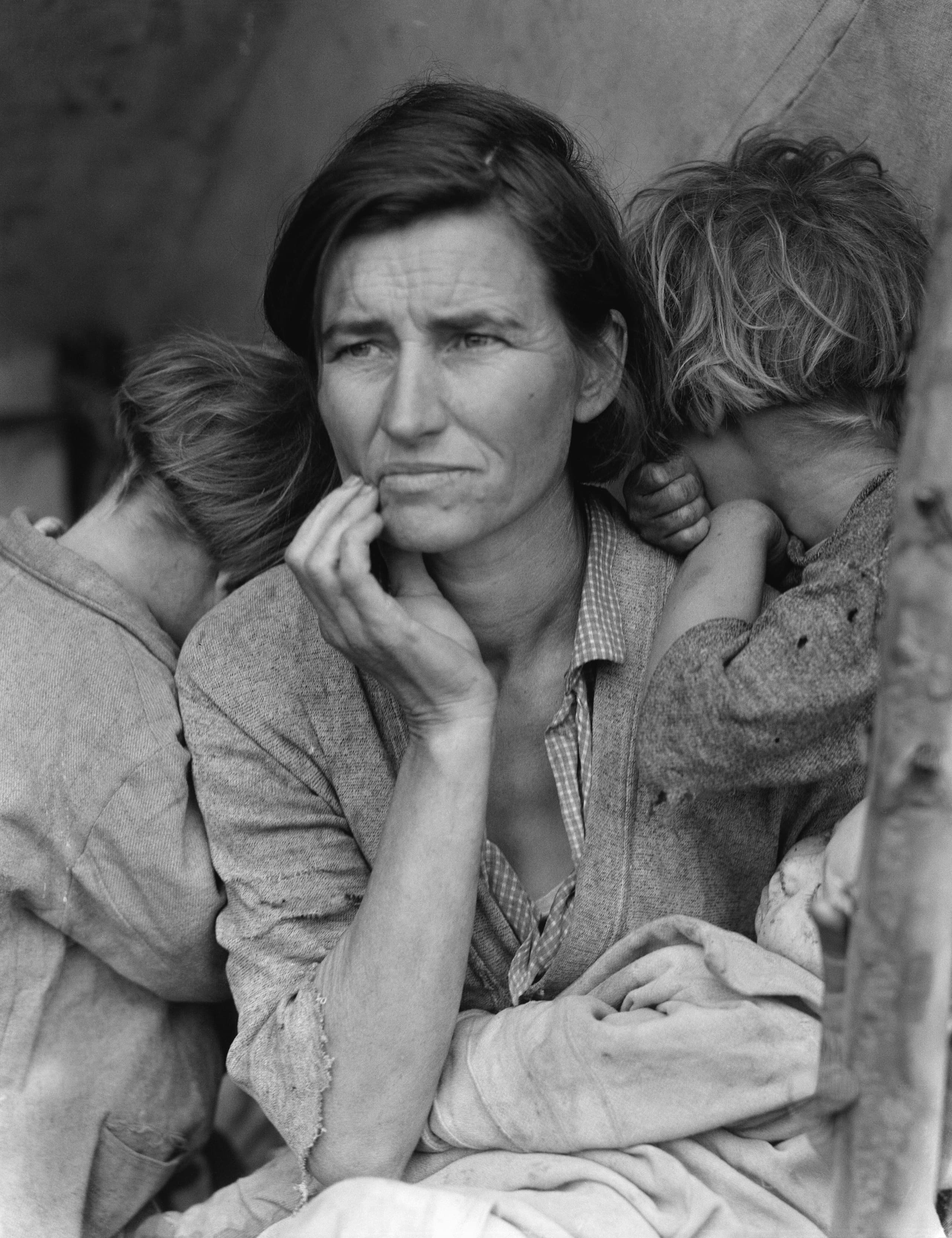 Black-and-white portrait of a seated woman looking past the camera, one hand raised to her cheek, an infant in her lap and two older children leaning against her with their faces turned away.