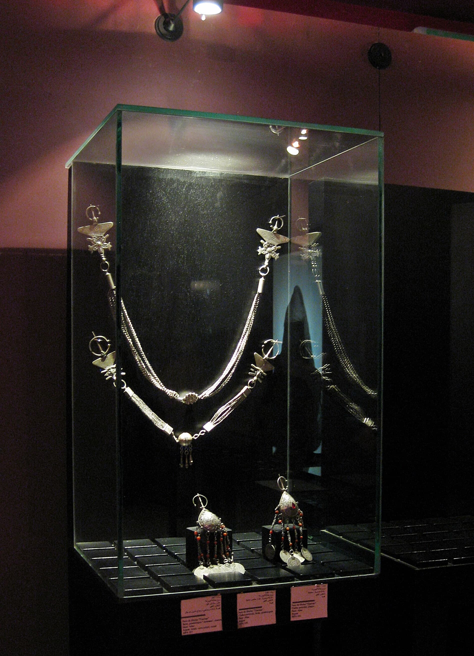 Silver jewellery including large triangular fibulae with geometric engraving, heavy necklaces, and bracelets, photographed against a neutral background.