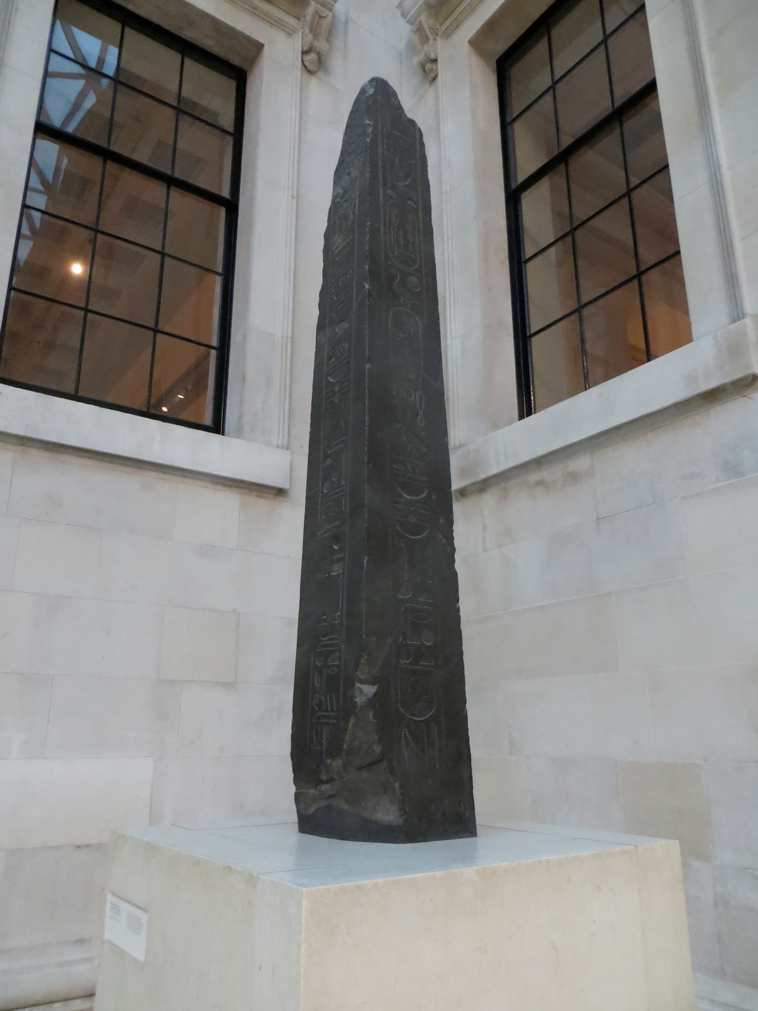 Two tall, broken granite obelisks standing upright in an indoor courtyard, their surfaces carved with hieroglyphic inscriptions, displayed on plinths with visitors visible nearby for scale.