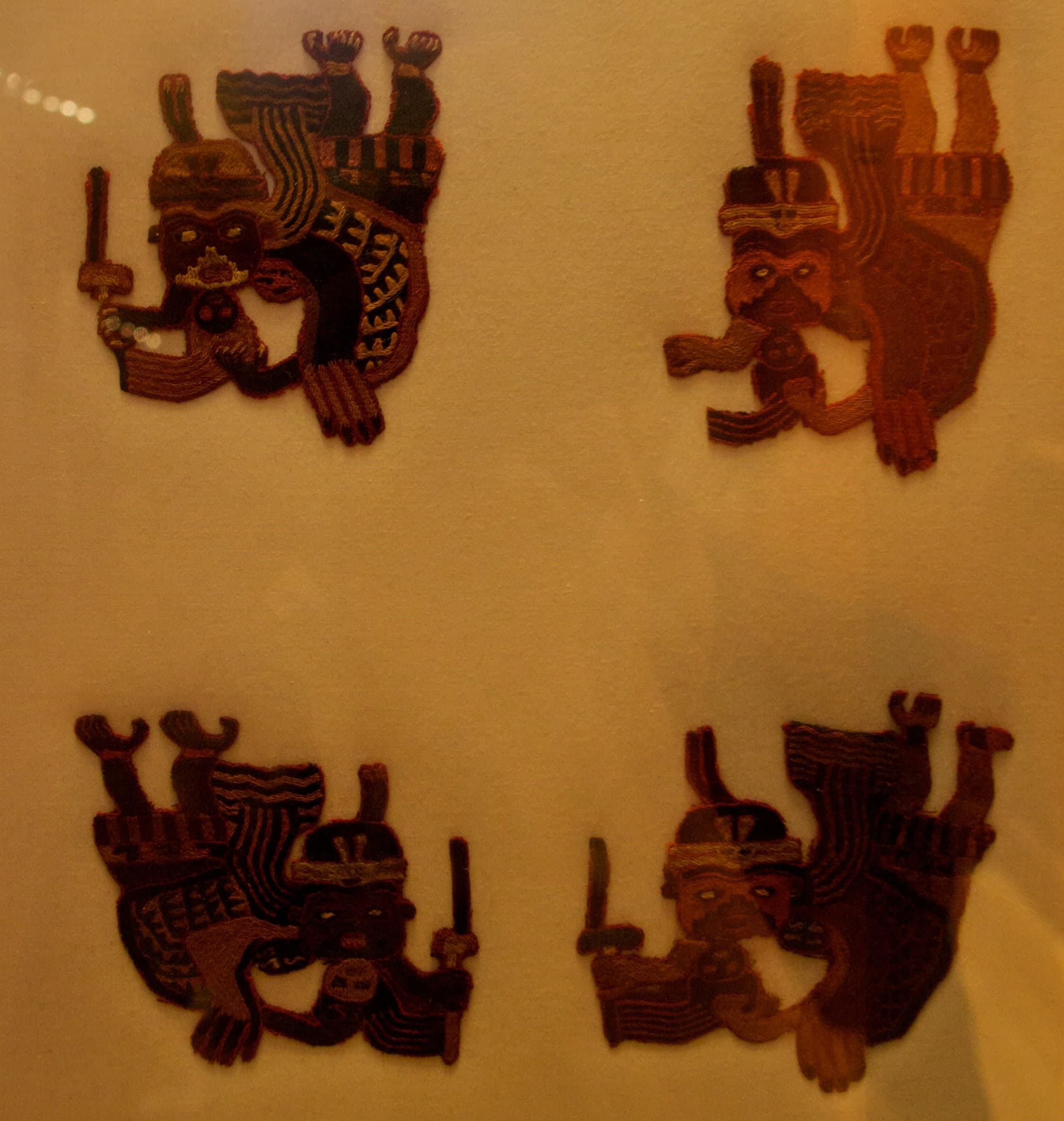 Embroidered textile with airborne human figures, each gripping a severed head by the hair, worked into the cloth in dense stitched detail.